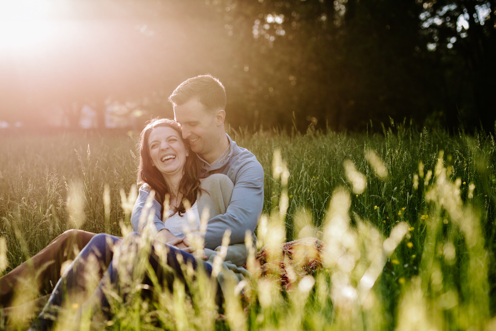 A man and woman sit together laughing in a sunny field of grass