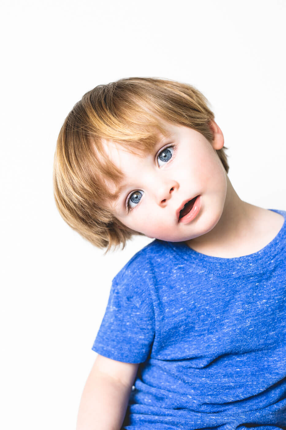 Young boy in bright blue shirt tilting his head in confusion