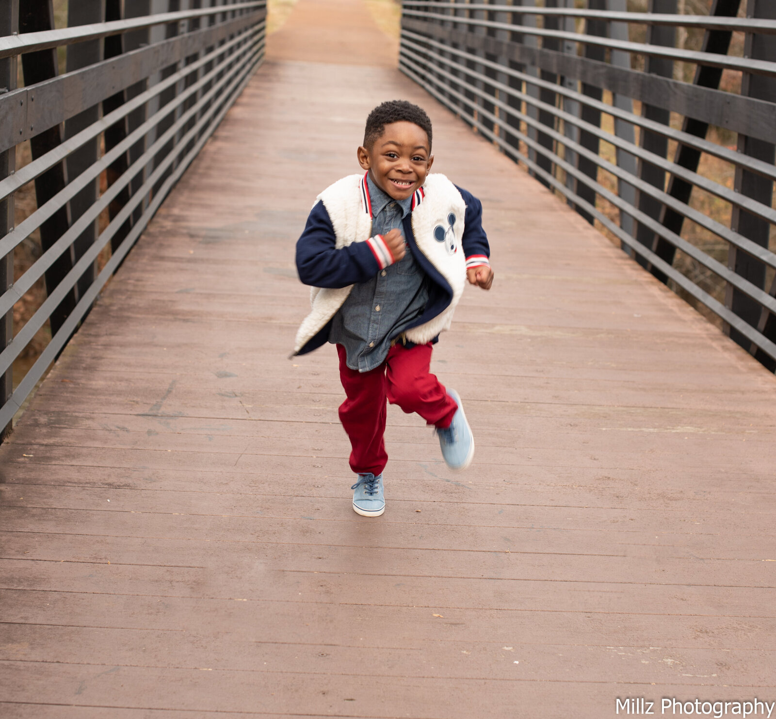 young boy running down a bridge while smiling at the camera photographed by Millz Photography in Greenville, SC