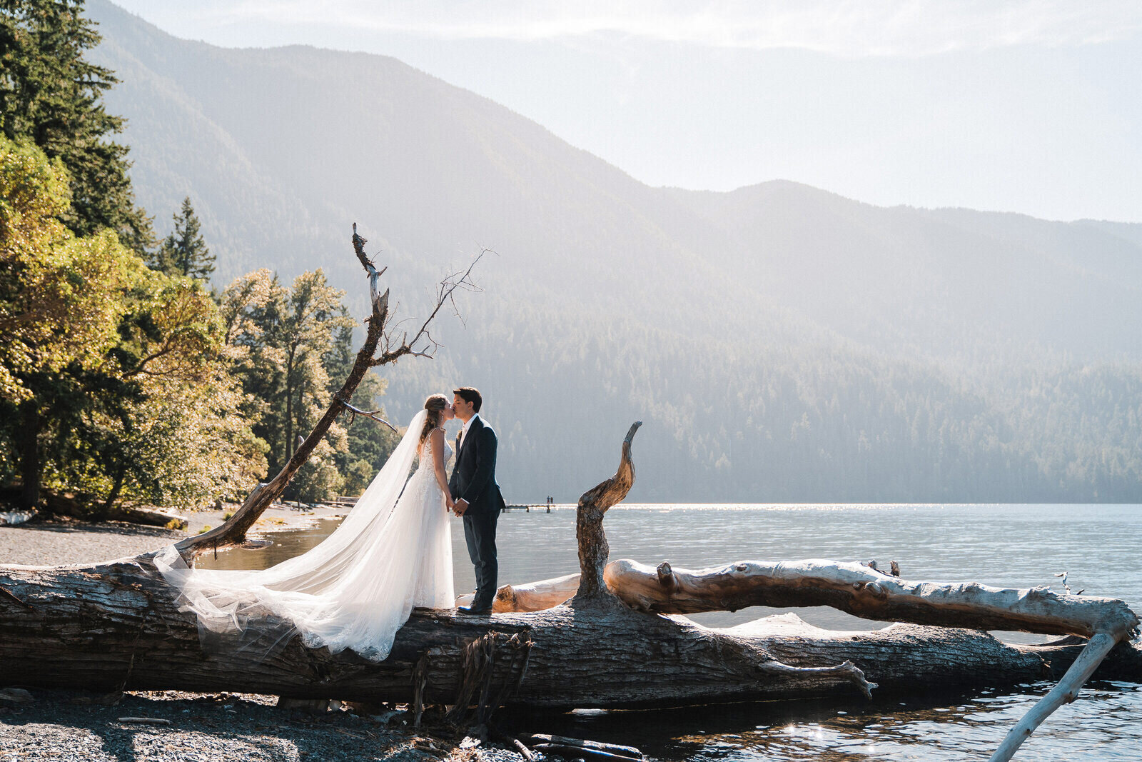 A couple stands and kisses on a log at Lake Crescent in Olympic National Park after their elopement