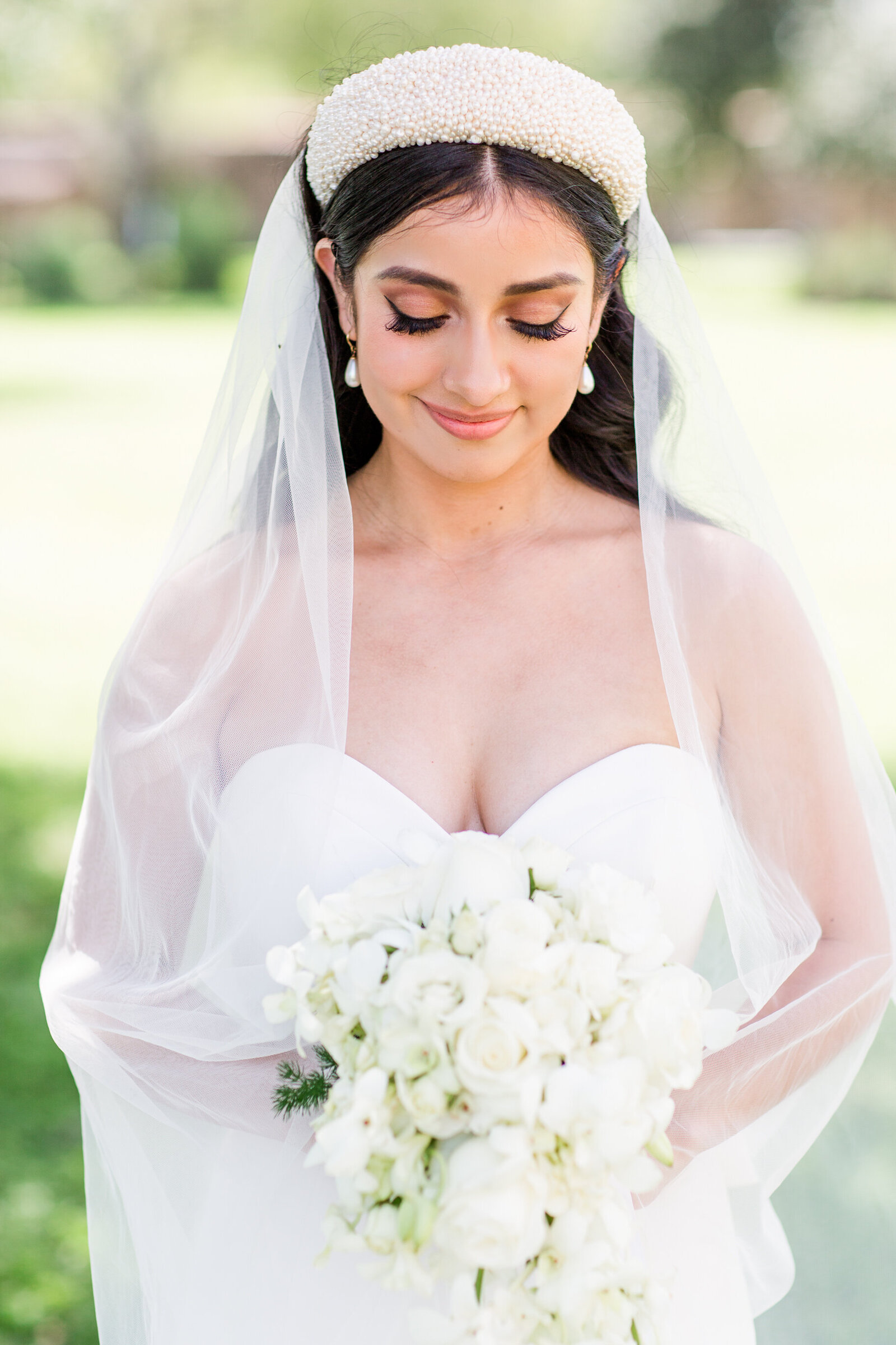 bride-outside-with-veil-over-her-shoulders-looking-down-at-her-bouquet