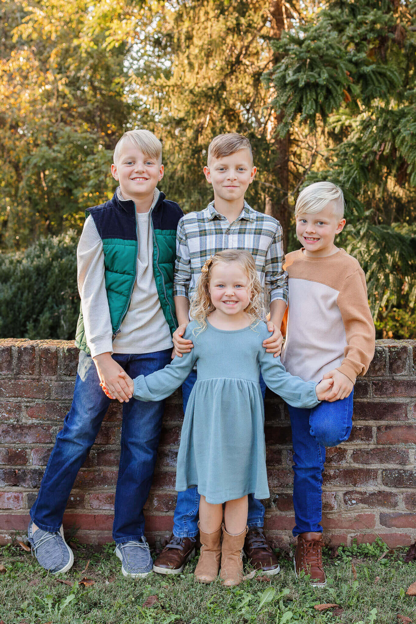 Four siblings standing up against a short brick wall.