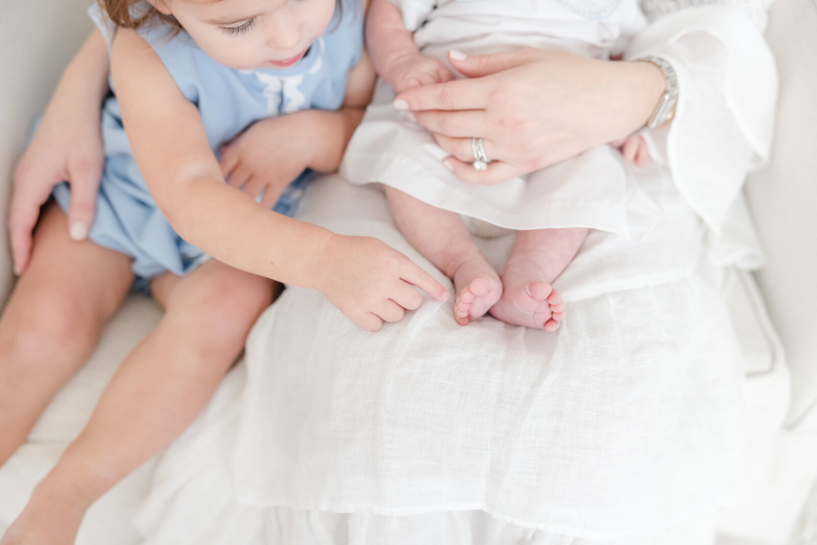 Toddler girl touching the toes of her newborn brother.