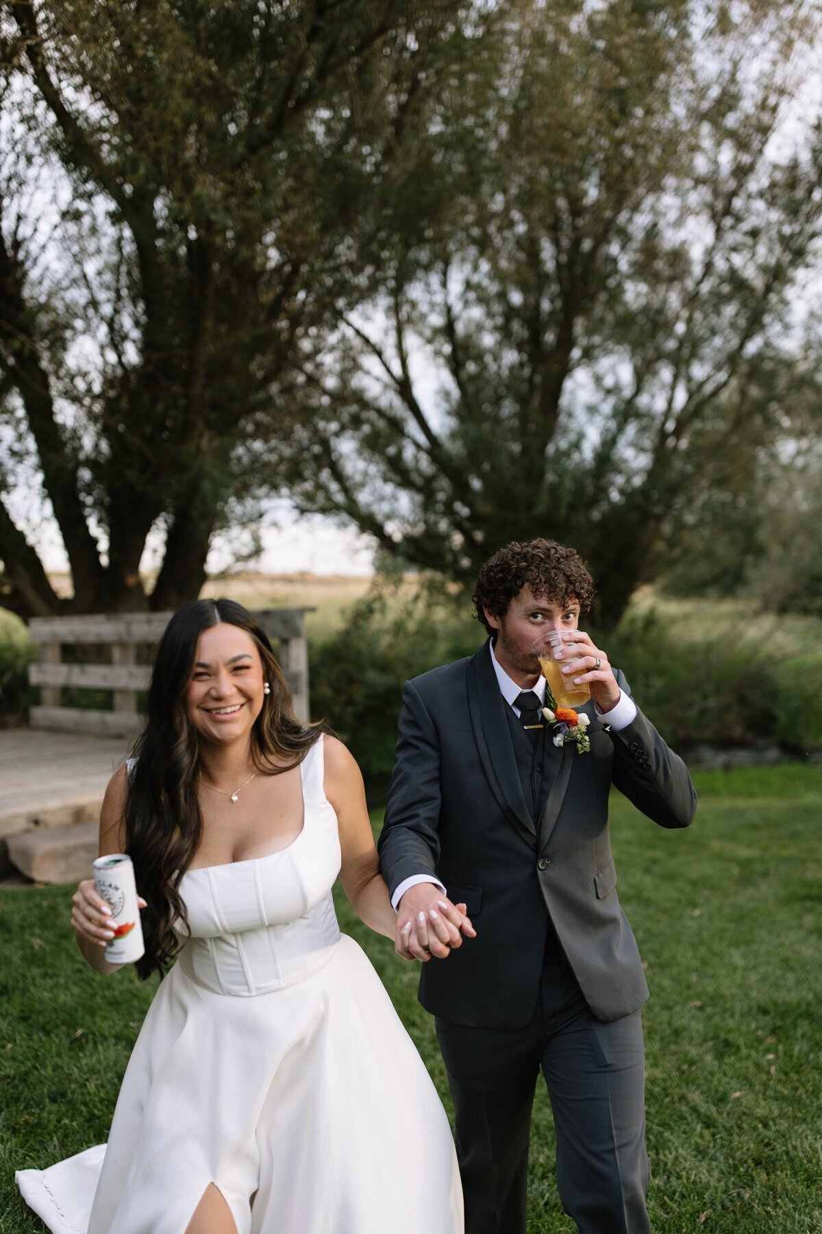 Bride and groom drinking white claws in park by destination wedding photographer