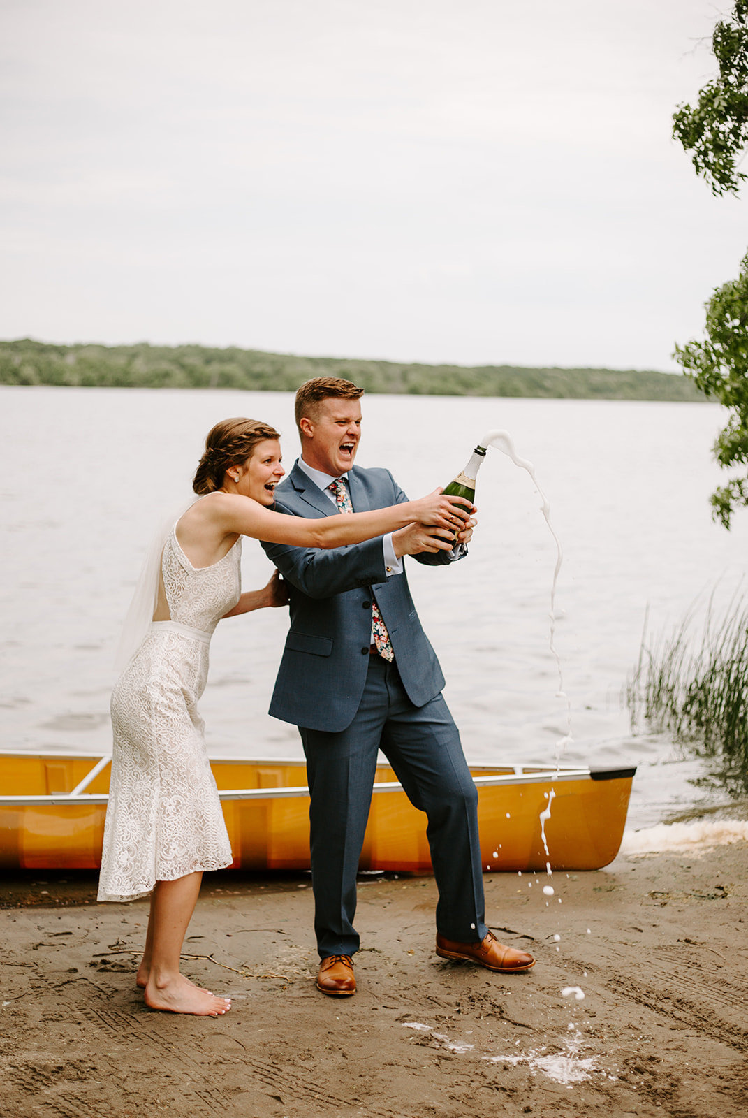 A Minnesota Bride and Groom popping champagne next to a lake and canoe on their elopement day