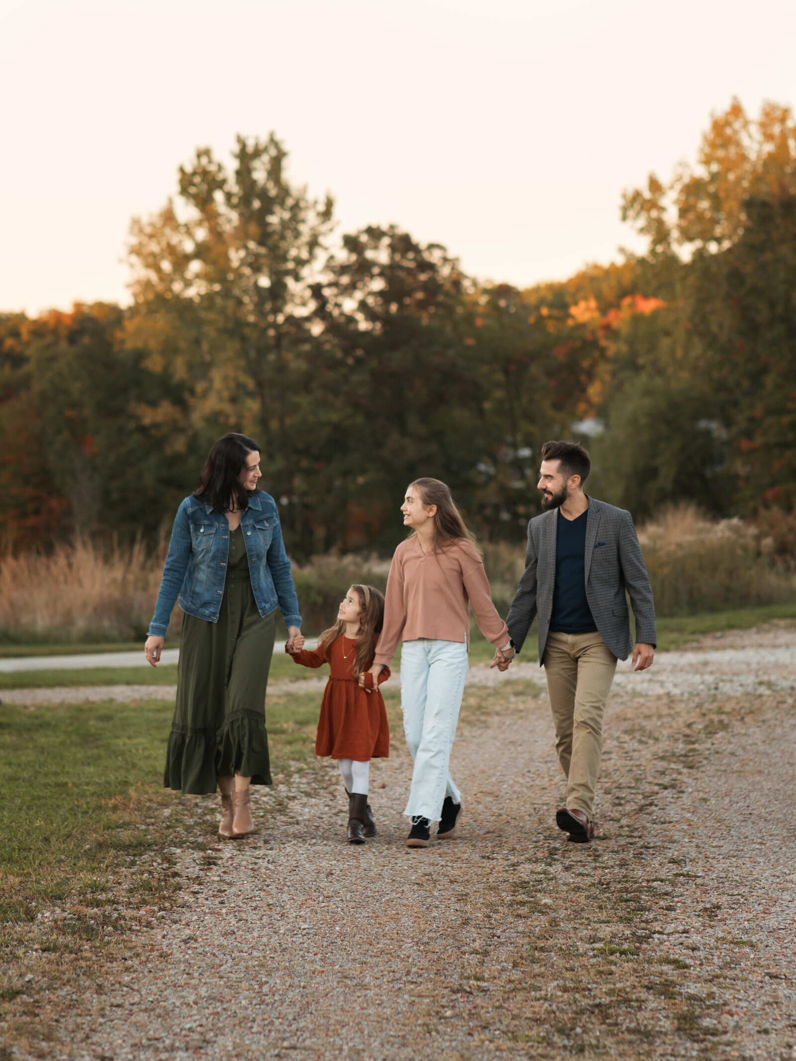 parents and two daughters holding hands and walking in park 