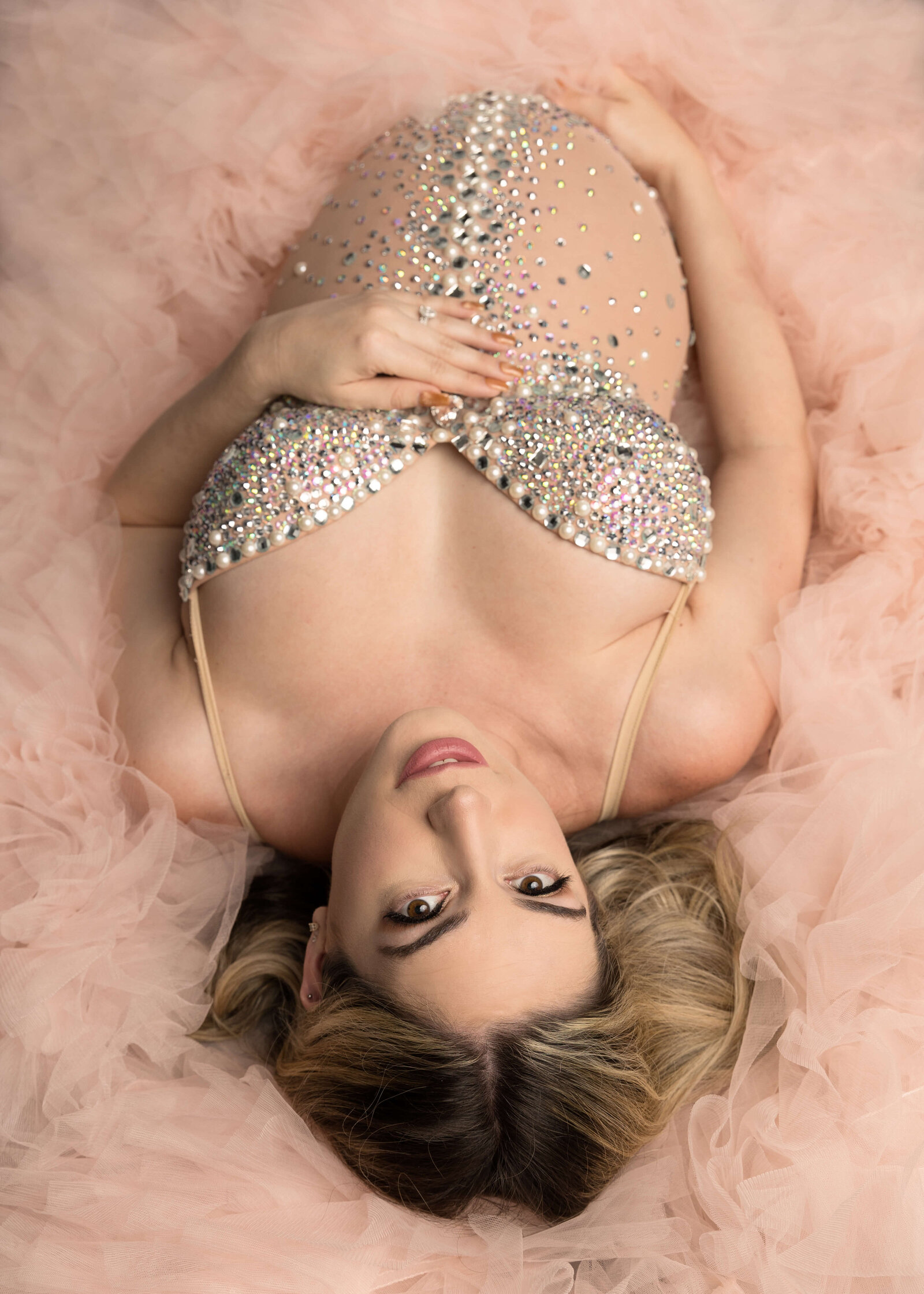 Expectant mom posed on floor wearing pink robe and jeweled bodysuit in studio by Ashley Nicole Photography.