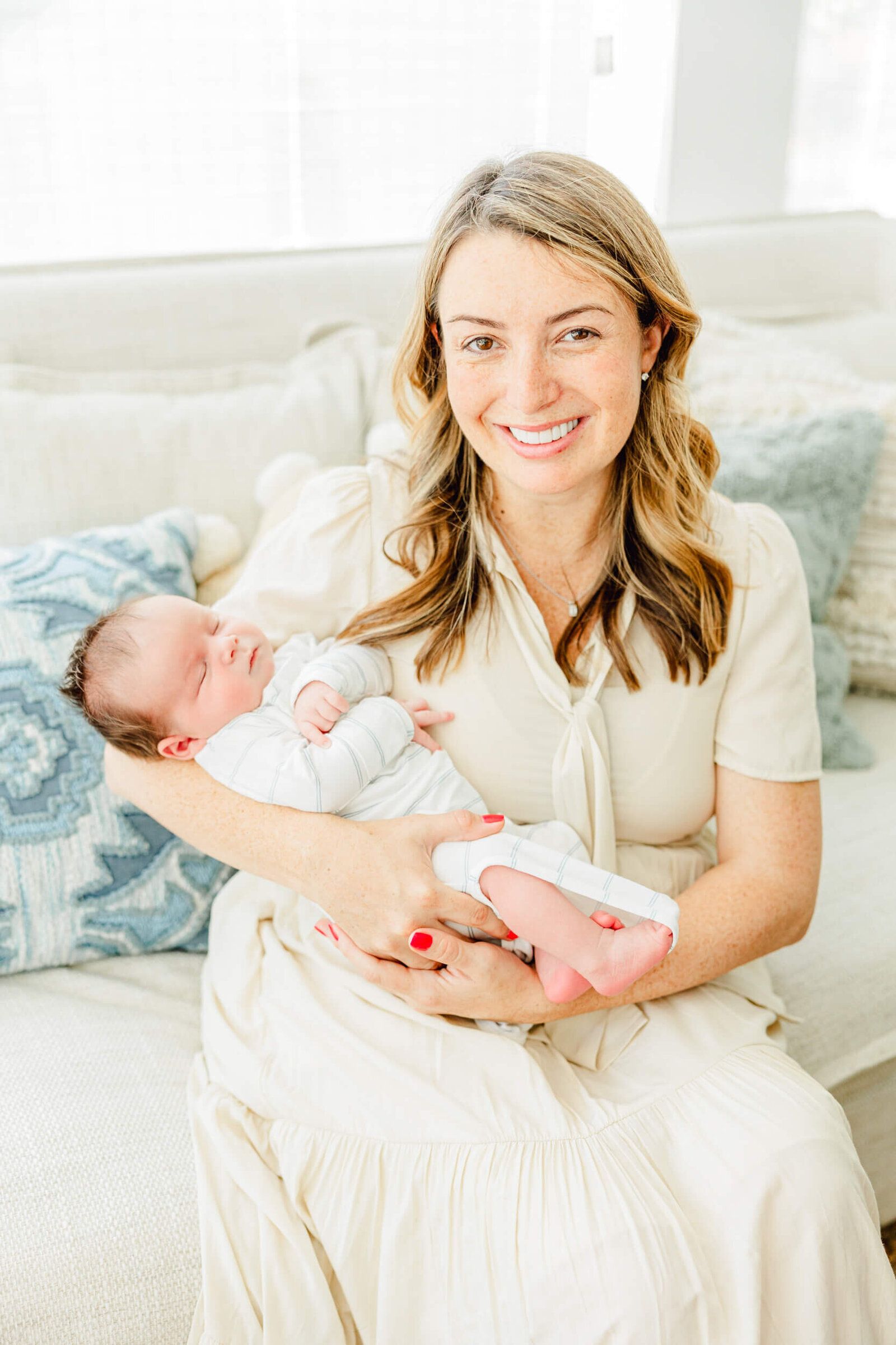 Mom sits on a couch and smiles while holding her baby