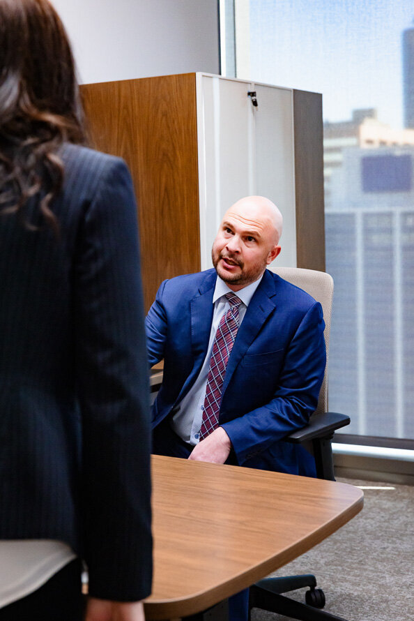Lawyer in blue suit jacket sitting at a desk talks to an employee.