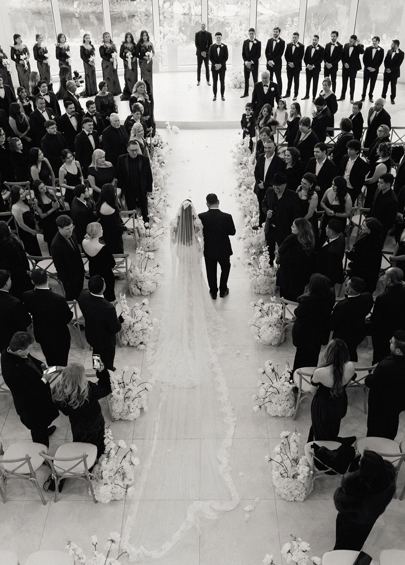 Bride walking down the aisle with her father as guests look on.