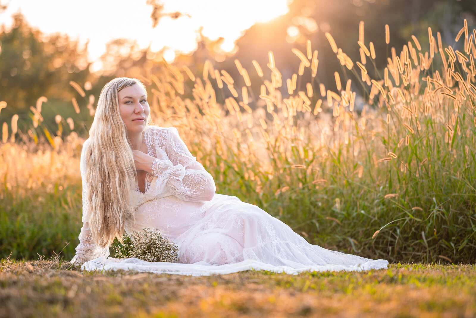 A pregnant woman sitting on the ground with golden grass behind her at the sun sets in Huntsville Alabama