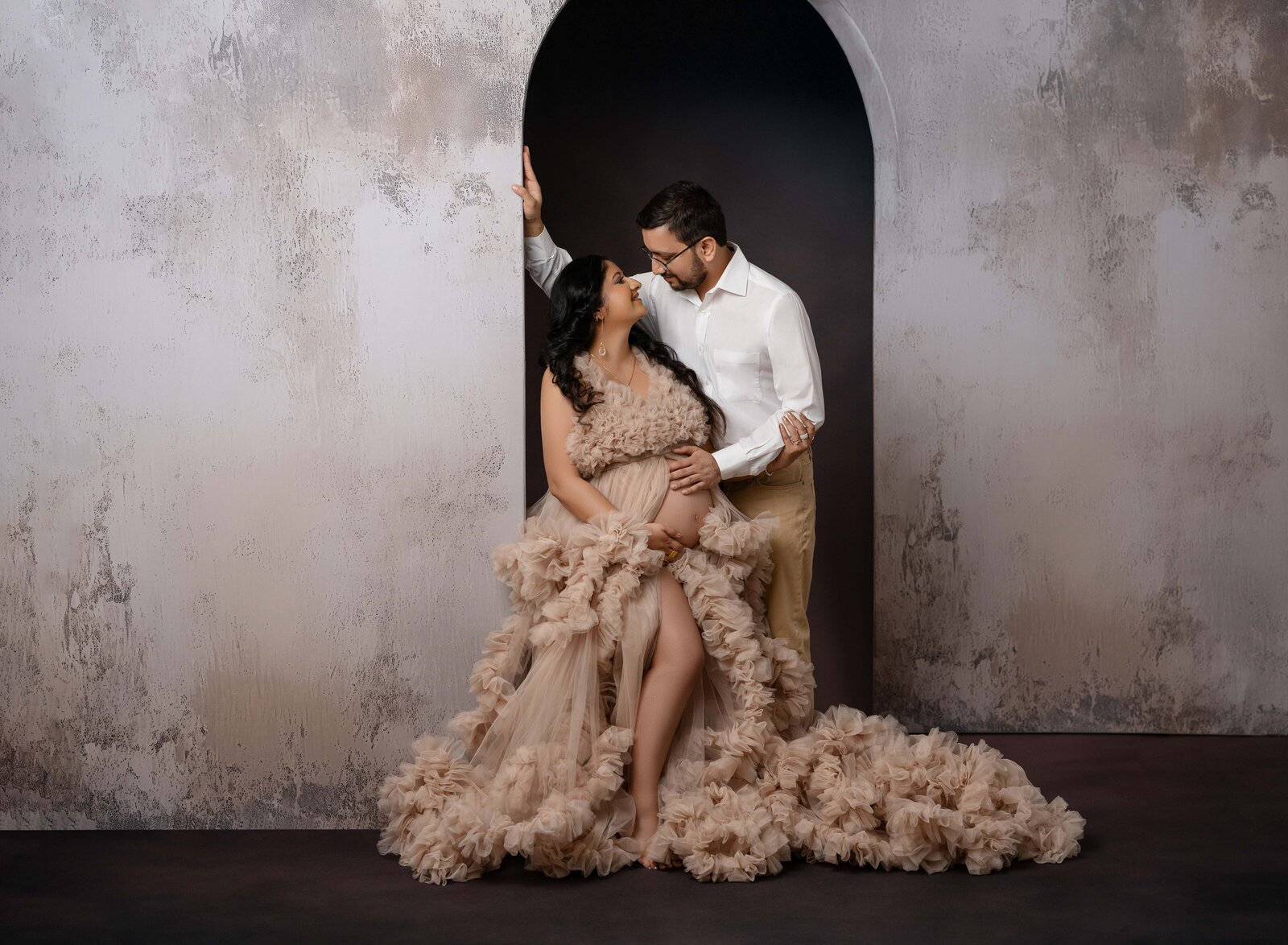 Maternity photo of couple looking at each other, leaning on arch walls. Photo taken at Atlanta Photo Studio.