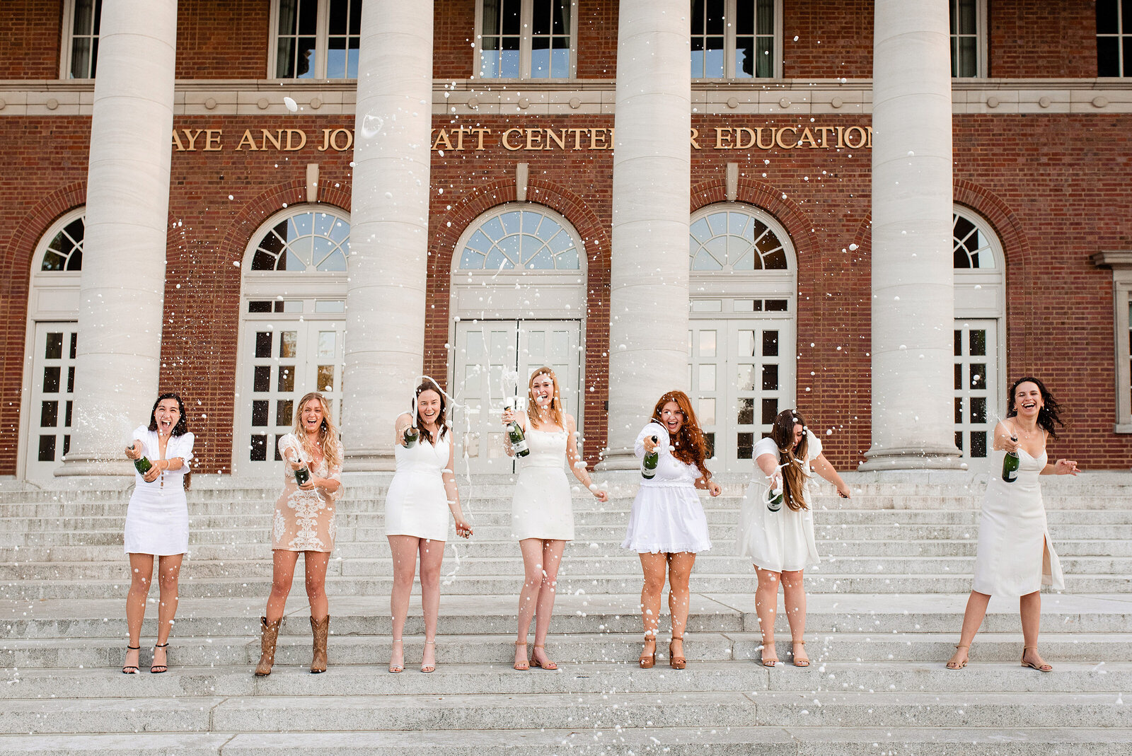 Seven seniors standing on the steps of Wyatt Center at Vanderbilt University, popping bottles of champagne while laughing