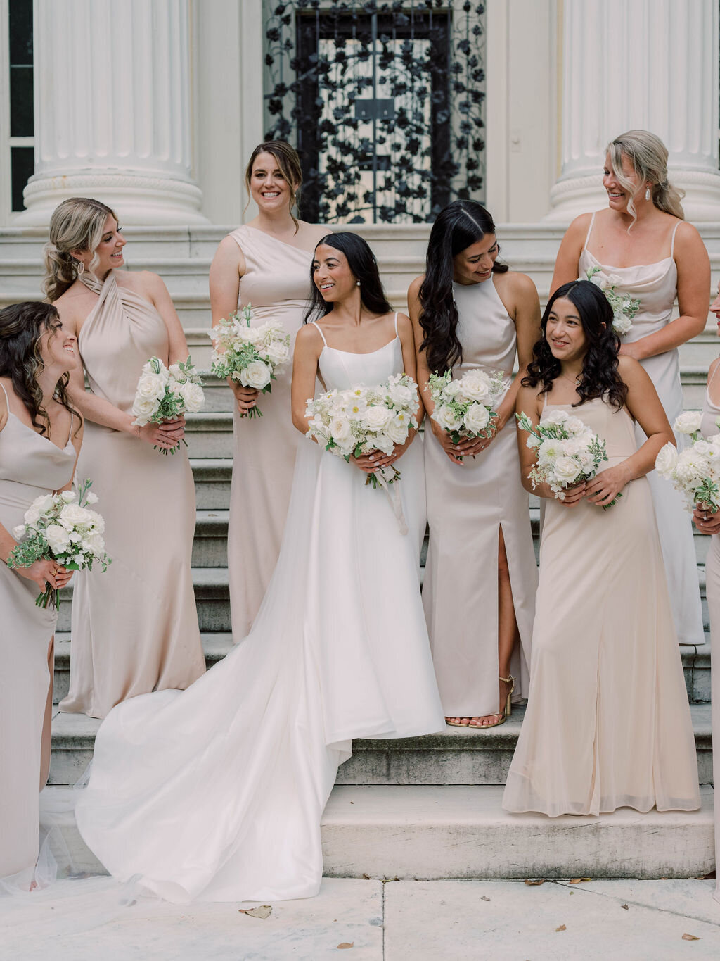 Bridal party holding white bouquets with white garden roses, white Japanese anemone, white dahlia, and white quick-fire hydrangea wearing champagne-colored silk slip dresses.