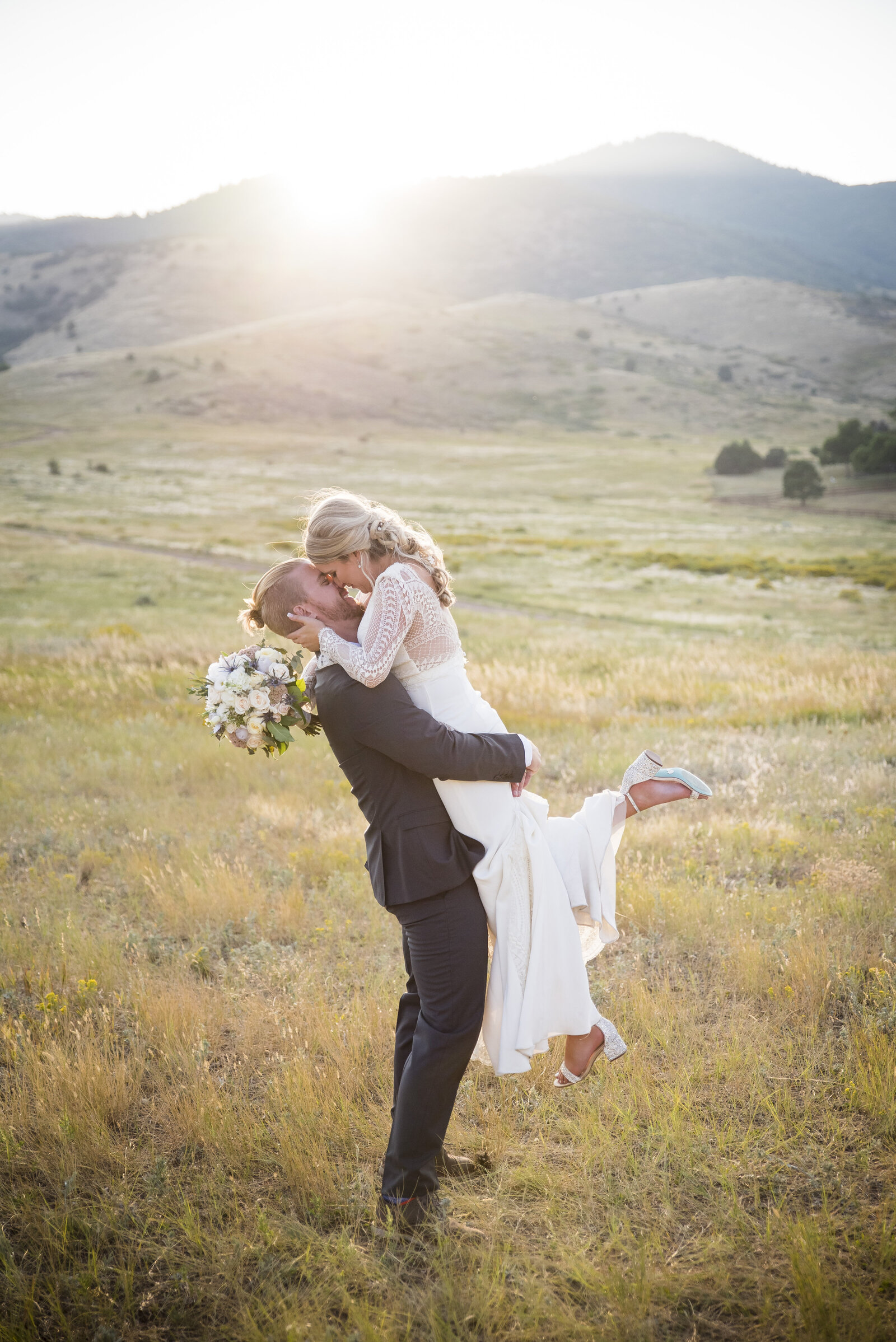 A groom lifts his bride off her feet in a field at golden hour at The Manor House in Littleton, Colorado.