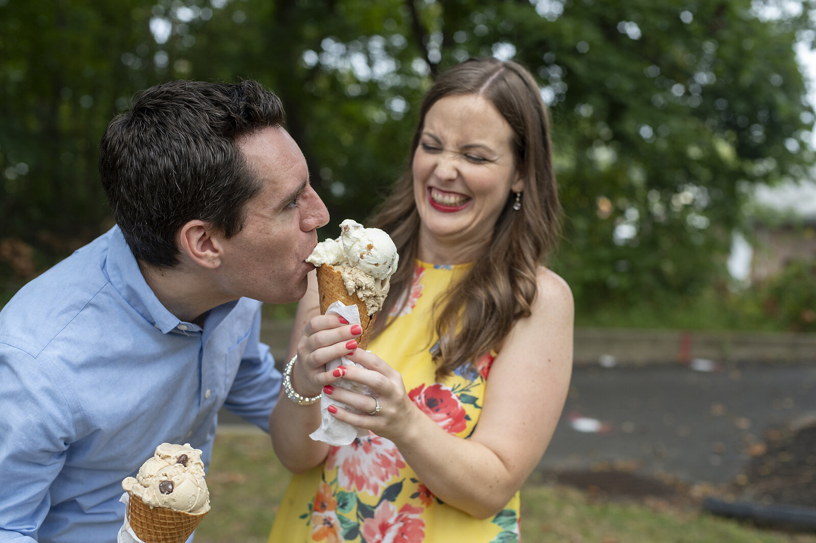 A couple laughing and holding ice cream as one takes a bit from the other's cone 