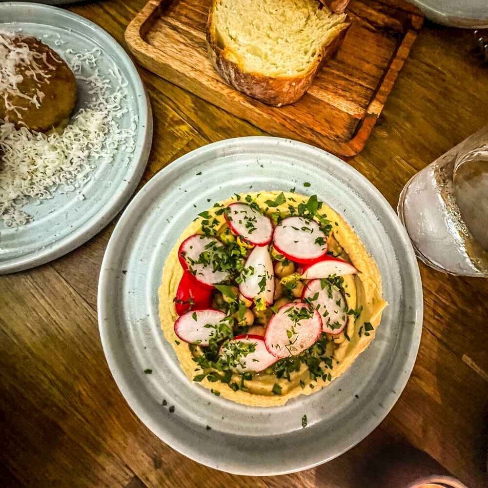 sliced radishes covering chickpea hummus on a plate with fresh bread on the side