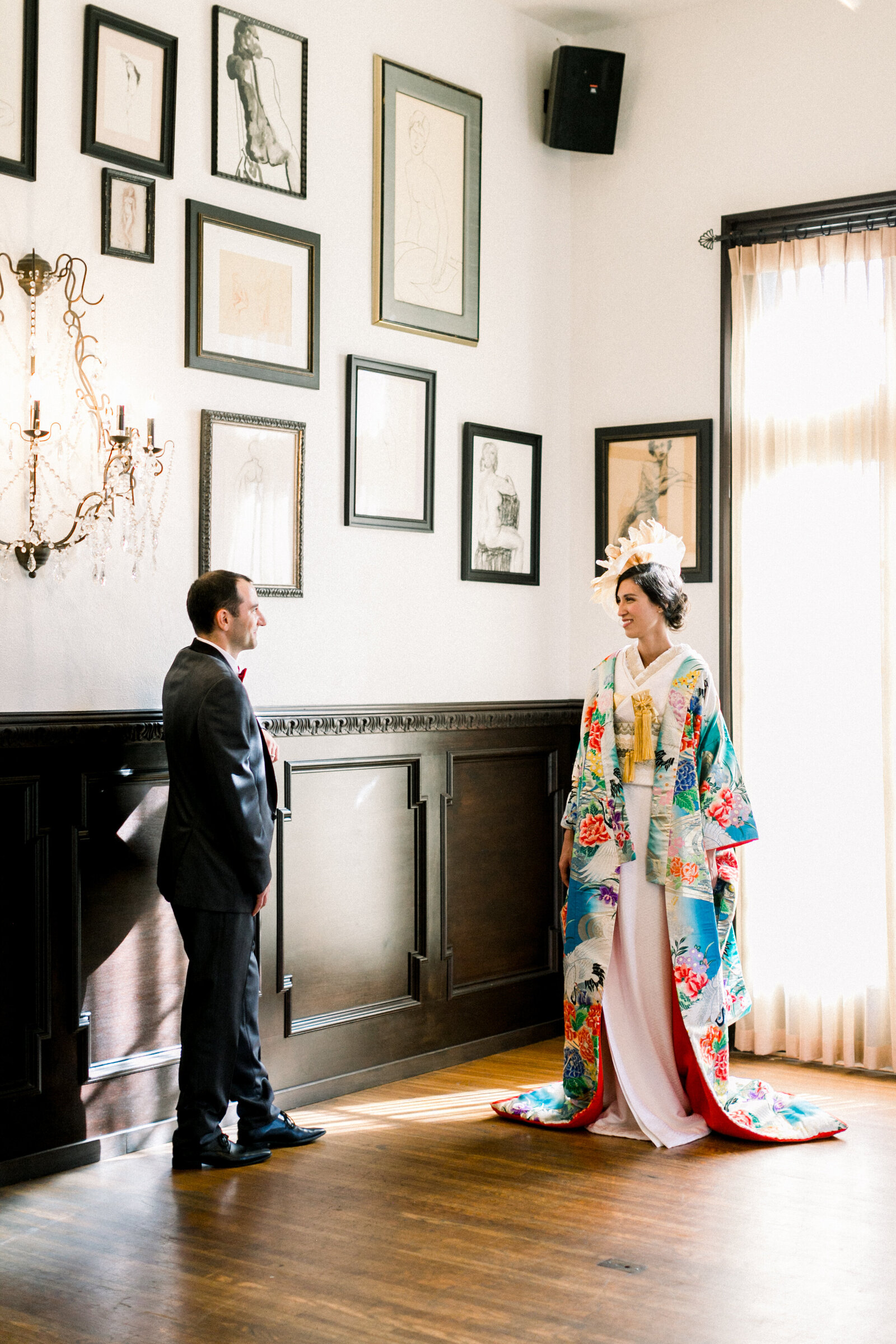 Bride in vibrant uchikake wedding kimono standing with groom in art-filled gallery at The Ebell Club Long Beach, perfect for wedding kimono rental in Los Angeles | ロサンゼルスのThe Ebell Club Long Beachアートギャラリーで鮮やかな色打掛姿の花嫁と新郎の着物レンタル前撮り
