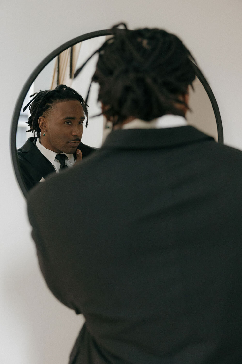 Groom in a suit adjusting his tie in front of a round mirror
