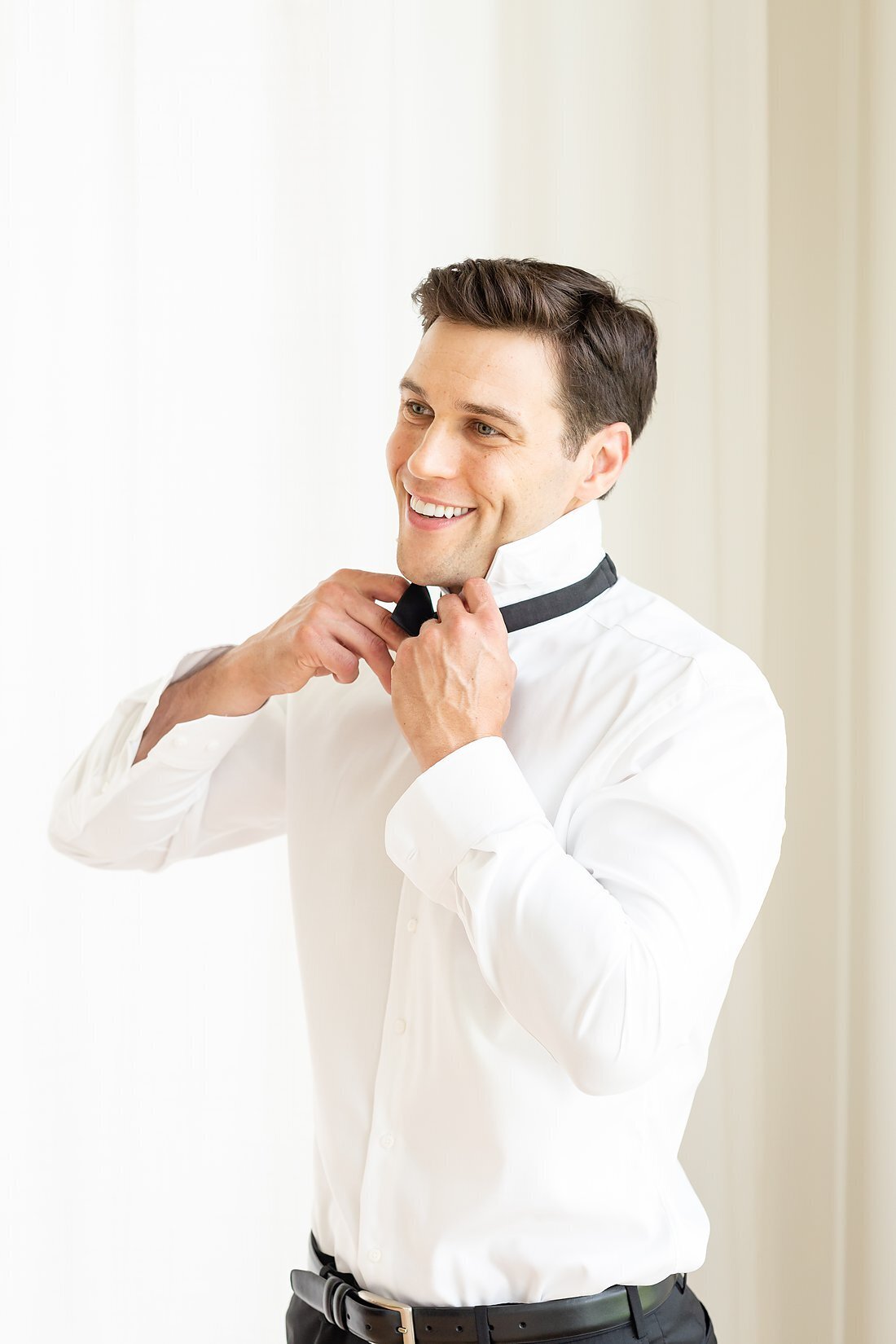 Handsome-groom-adjusts-his-bowtie-on-his-wedding-day