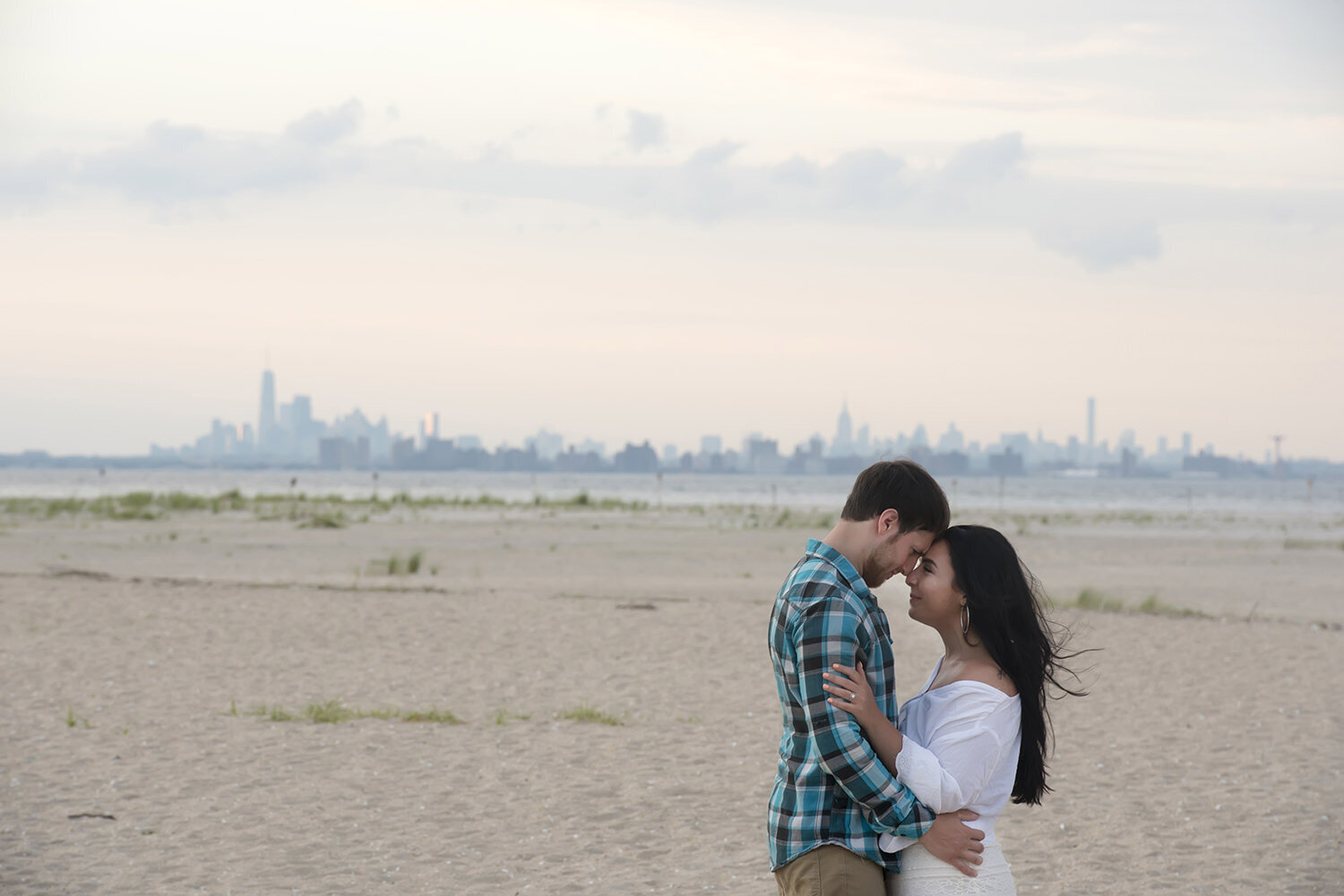A couple standing close with their heads together as they stand on a beach 