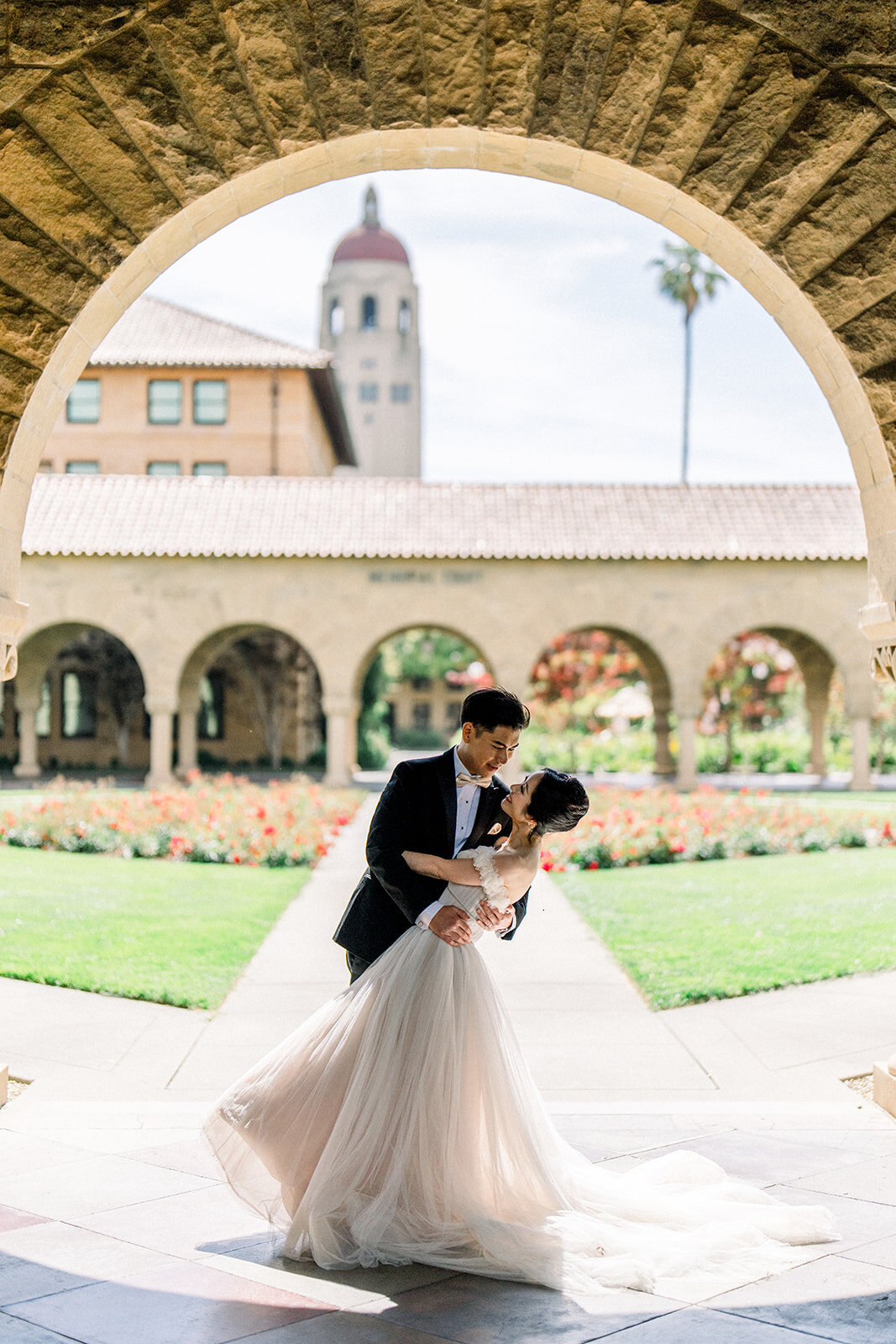 The bride and groom share a romantic dance in the picturesque courtyard of Stanford University, highlighting their love and joy.