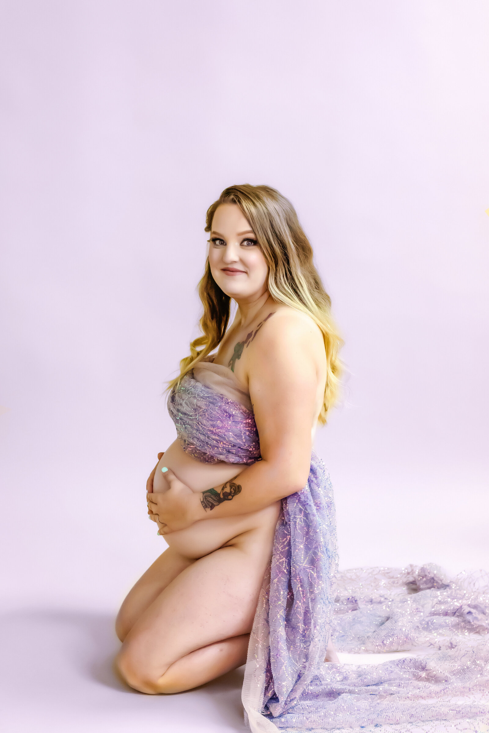 Maternity Photographer, a woman kneels , she is pregnant, covered in a blanket