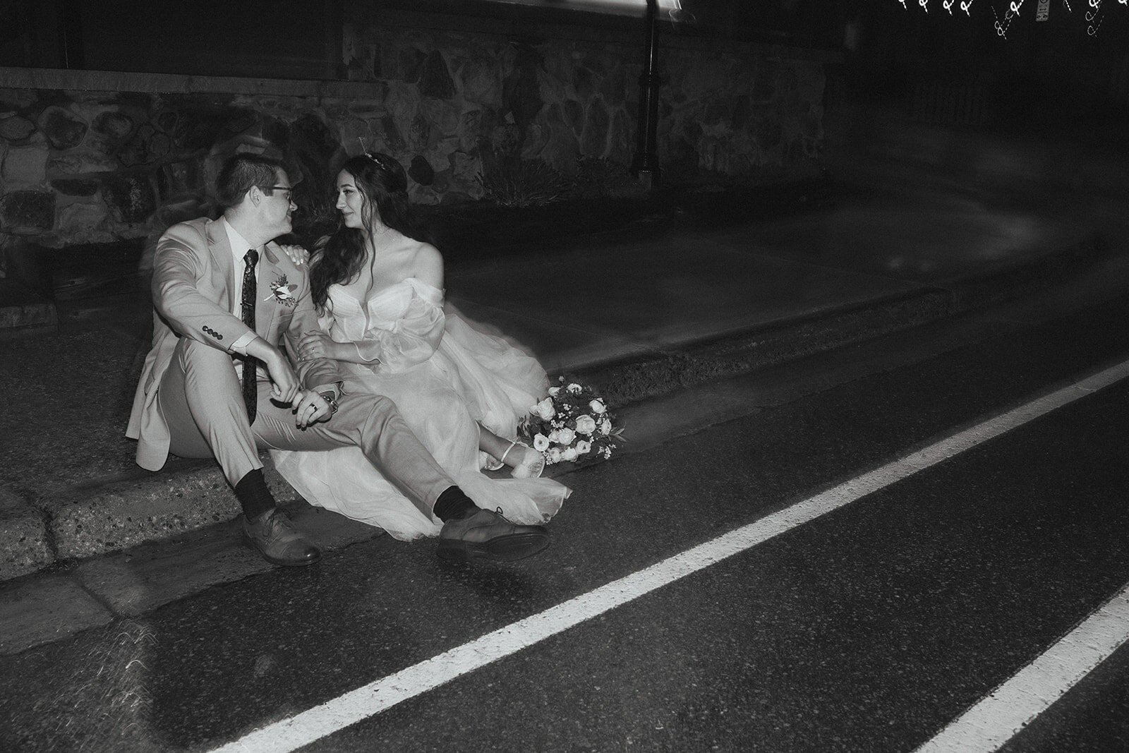 Black and white photo of married couple sitting down beside the street