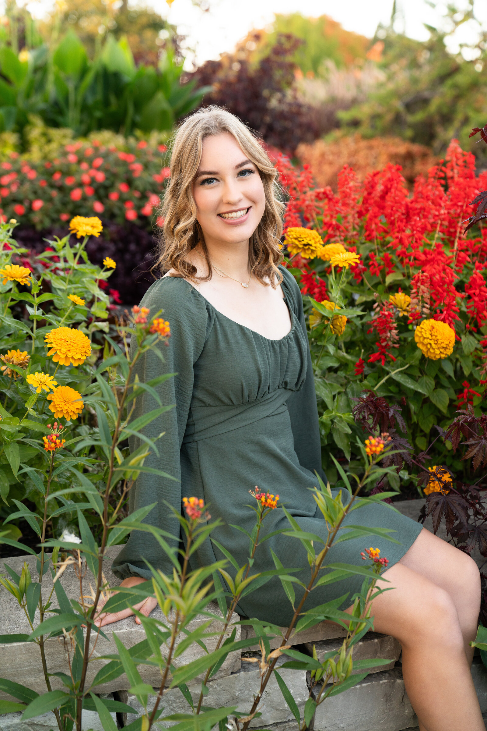 High school girl sits on a ledge surrounded by flowers during her senior photo session at the Minnesota Landscape Arboretum in Chaska, Minnesota.