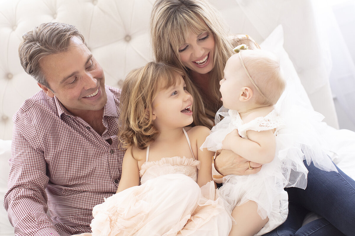 Parents tickle children playfully on bed in Dallas Family Photography studio.