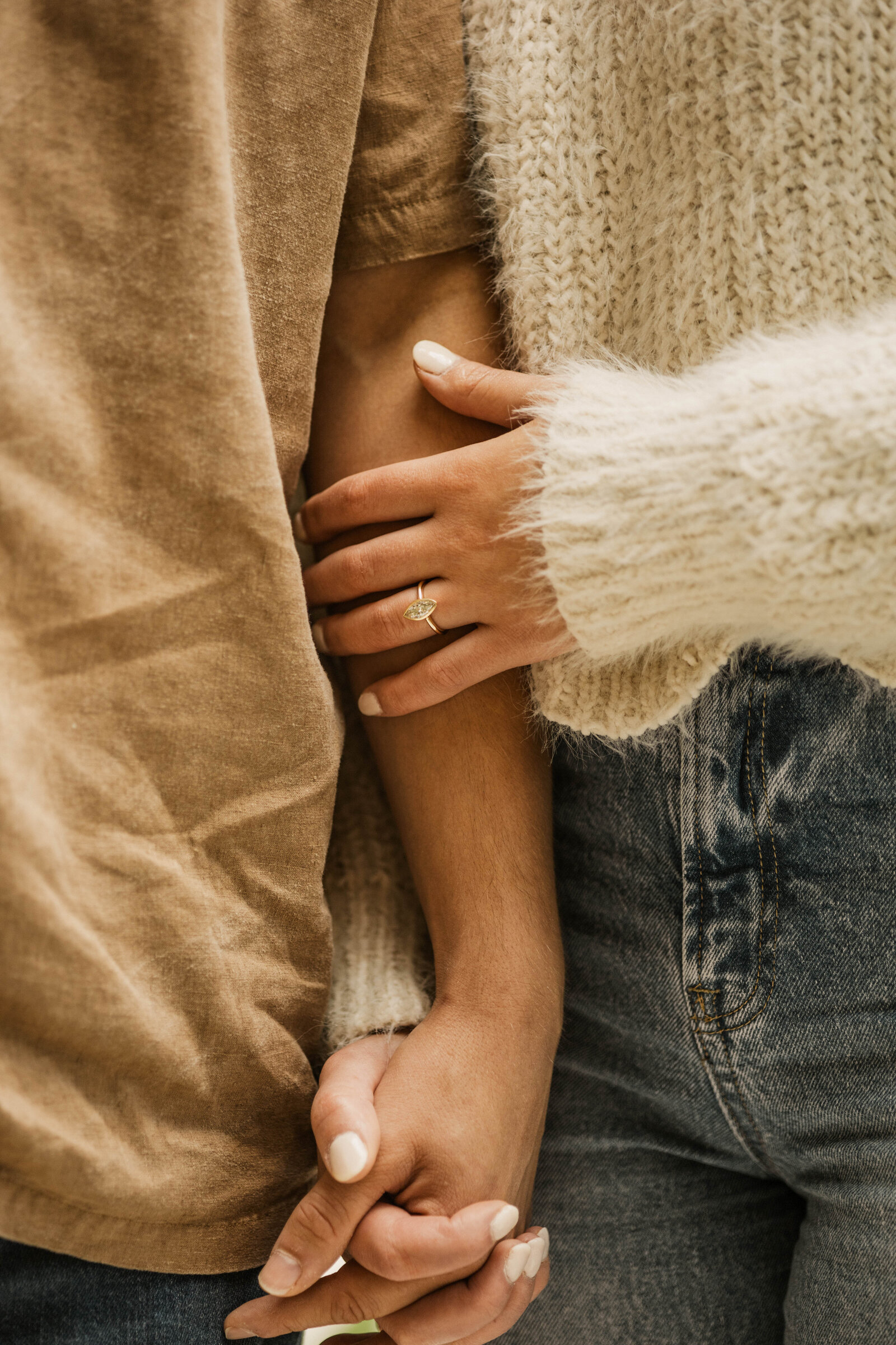 Close-up of a couple holding hands during their engagement session, with a focus on her engagement ring, showcasing the connection.