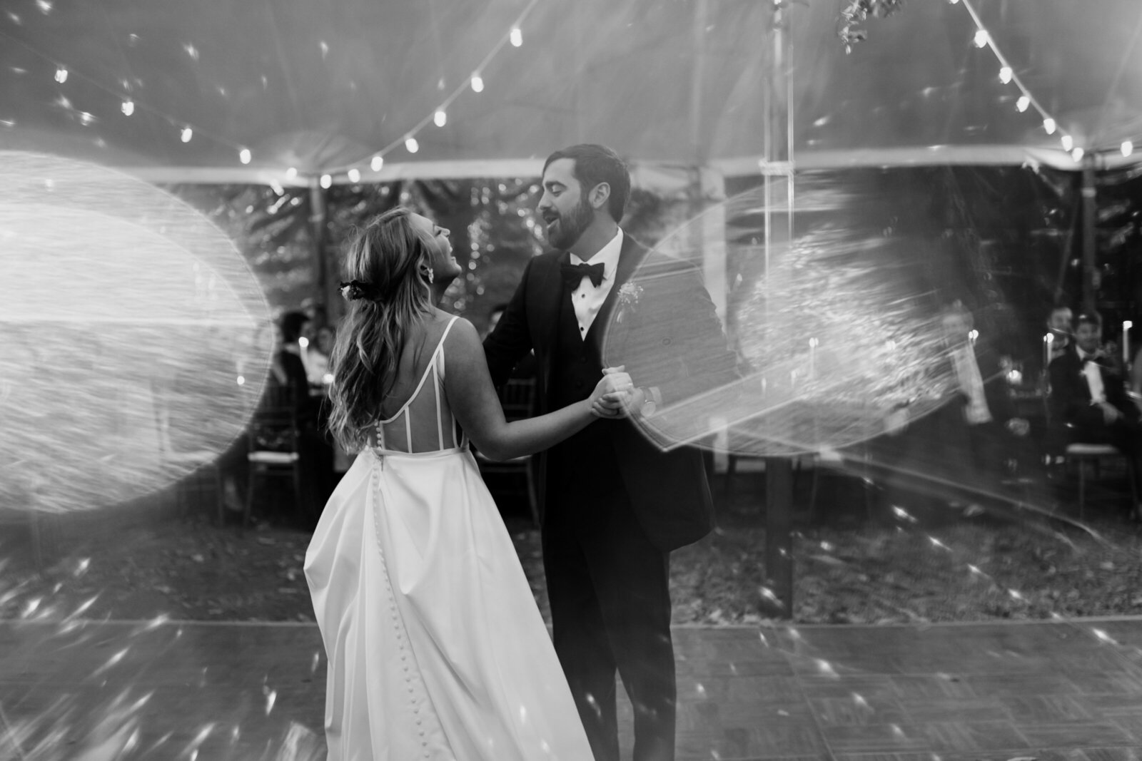 A bride and groom dance under twinkle lights in a large tent