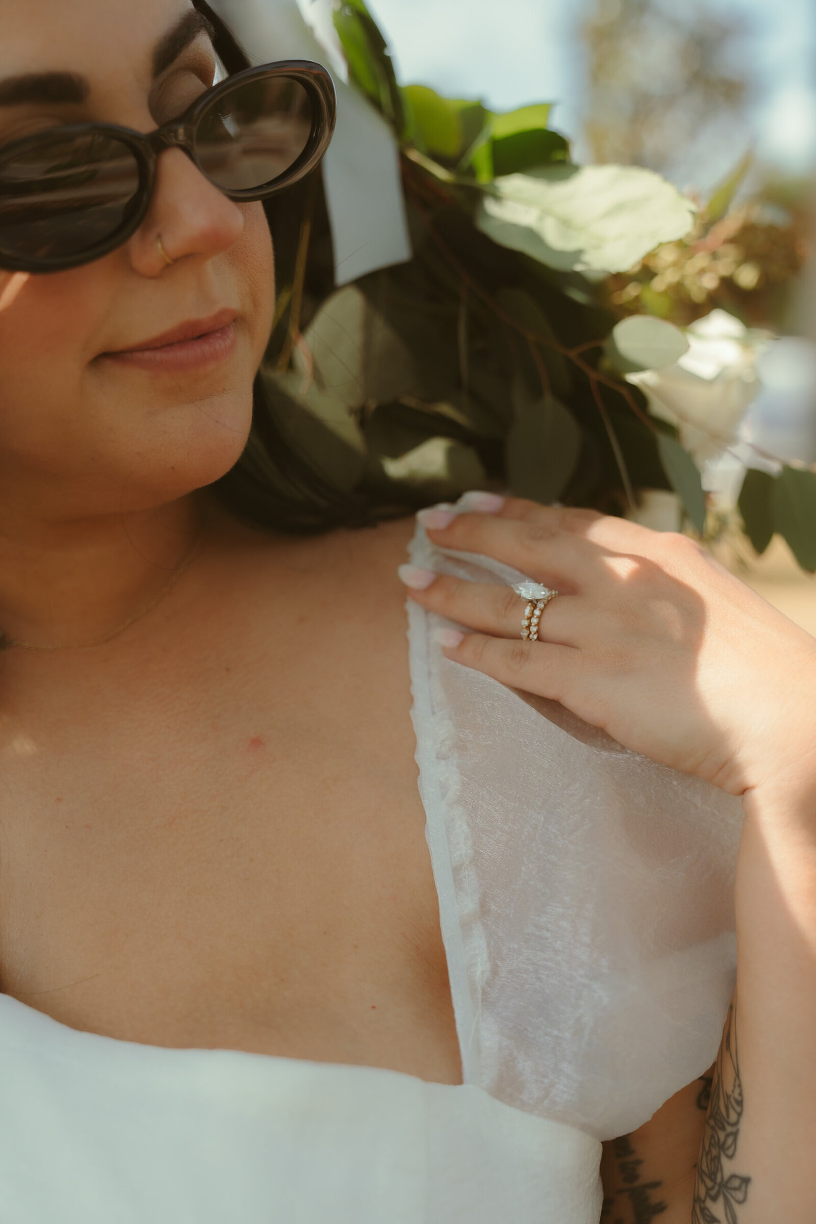Close-up of a stylish bride wearing sunglasses, showcasing her engagement ring and boho bouquet.
