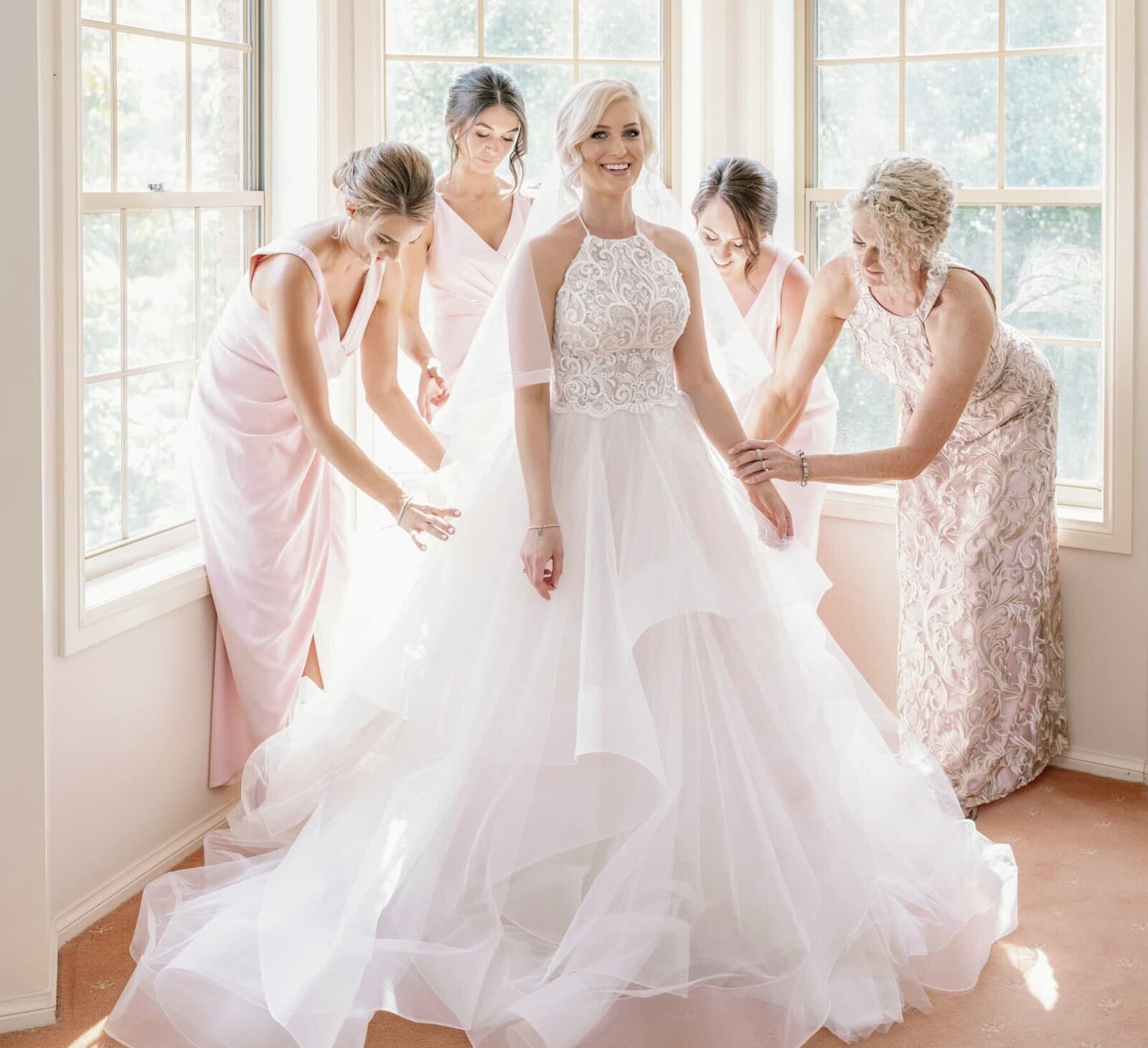 Bridesmaids are helping bride get dressed in her Oksana Mukha bridal gown