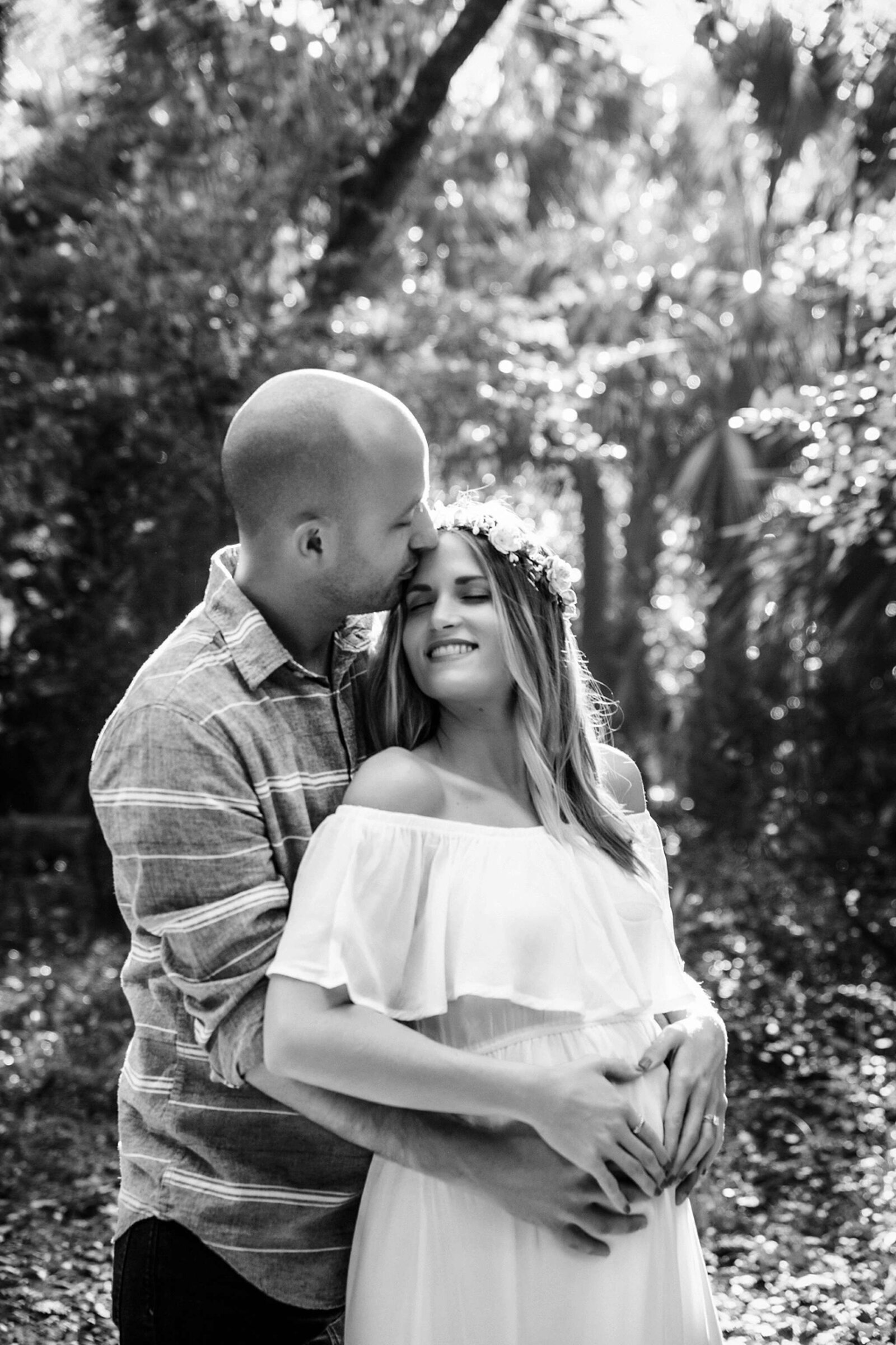 A loving moment in the woods as a pregnant woman hugs her husband, captured by Orlando's best maternity photographer.