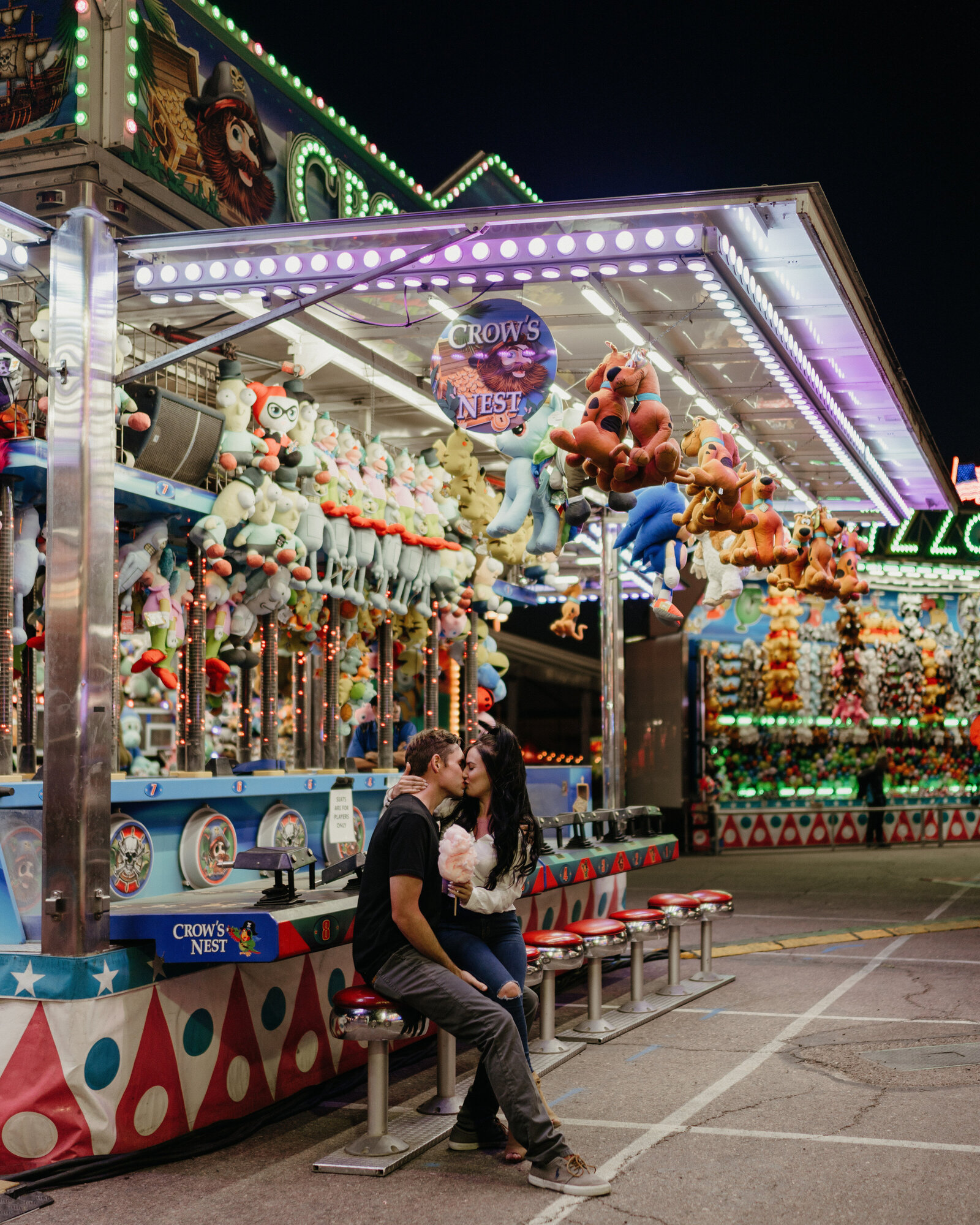 A couple share a kiss while at a carnival.