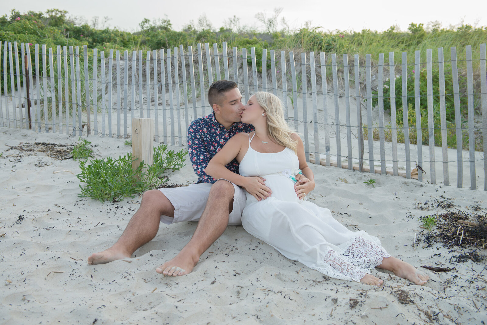 Husband and wife kissing in maternity photo on beach