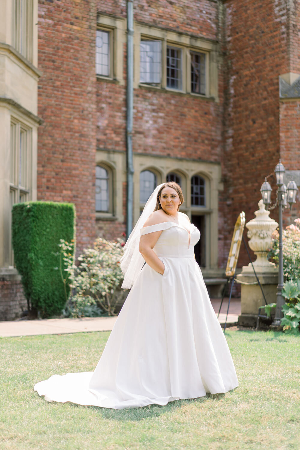 A bride in an off-shoulder gown with pockets, posing in a garden