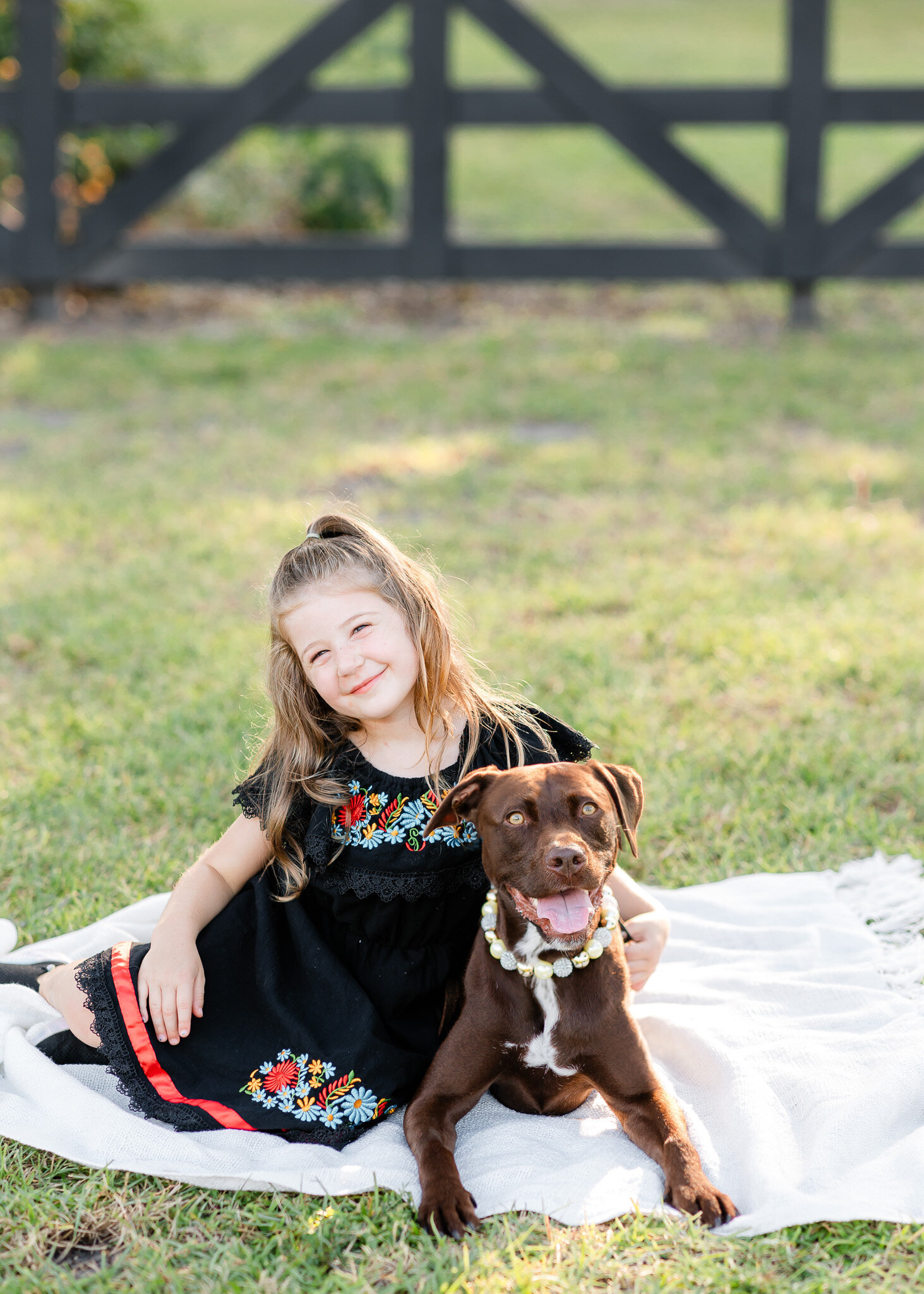 Little girl wearing a black dress sitting on a blanket with her dog