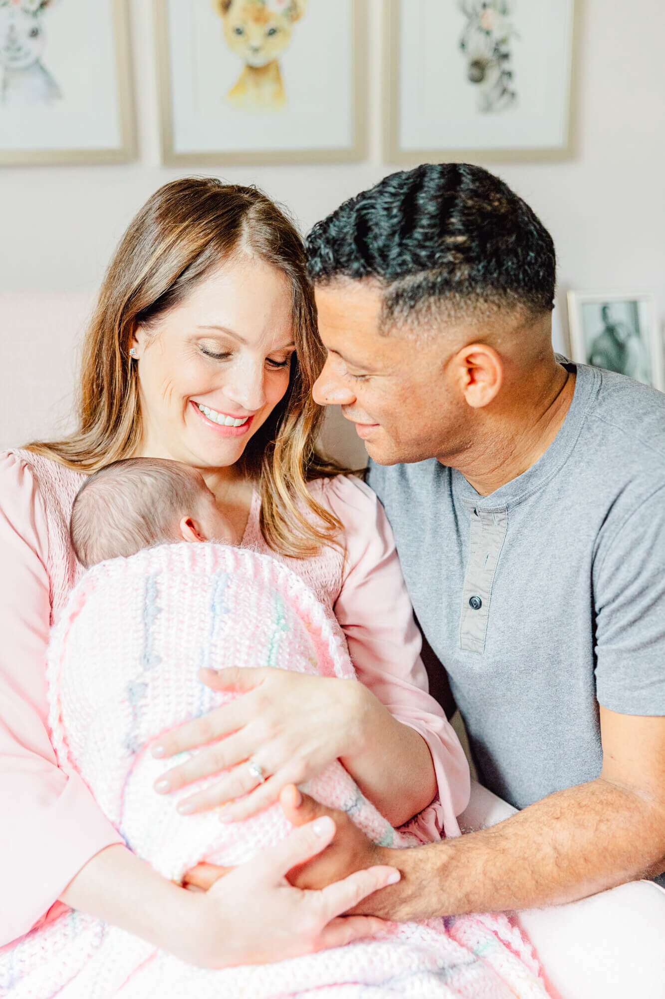 Mom smiles at baby in a pink blanket while dad smiles at mom