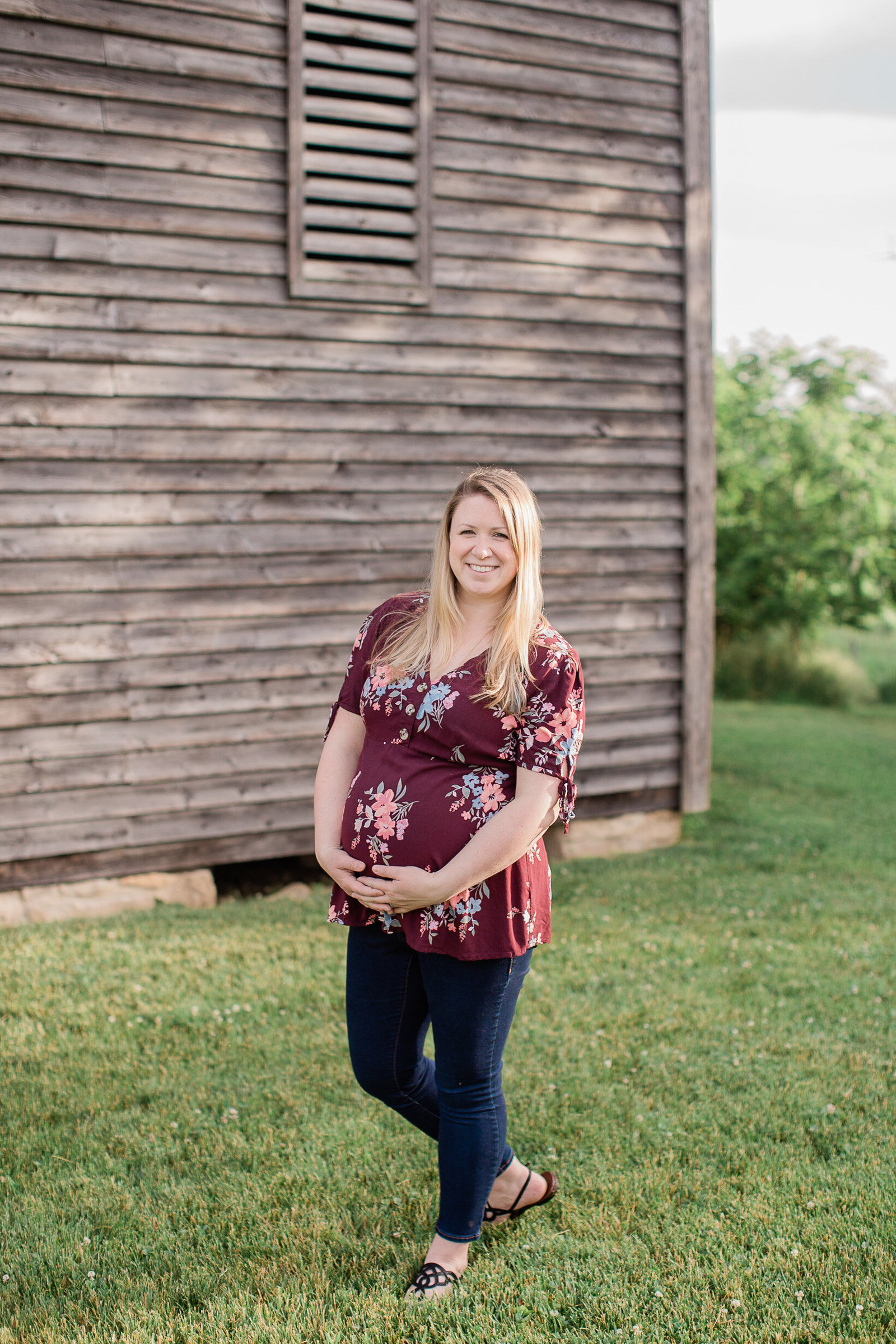 Blonde pregnant mother standing in front of a building in red flower shirt, holding her baby bump