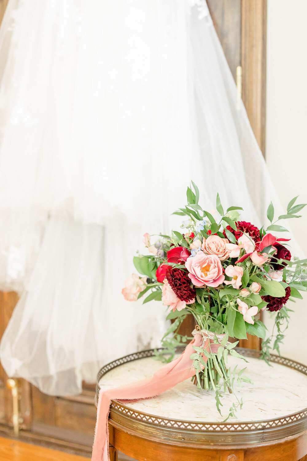 Bridal bouquet with pink and red flowers beside wedding gown