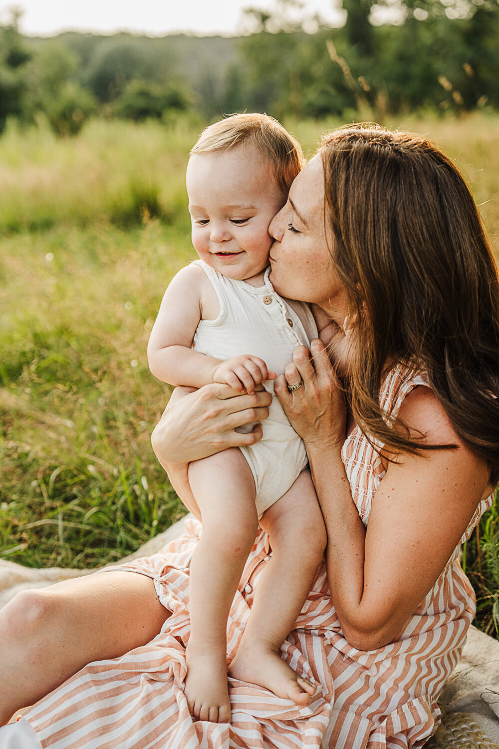 mom in striped dress snuggles baby boy at sunset