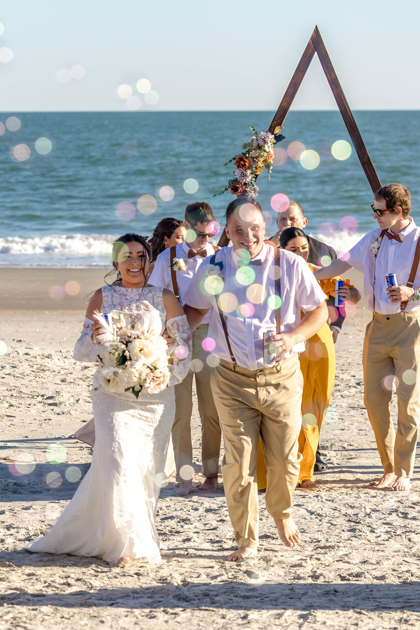 A joyful couple celebrating their beach wedding ceremony at Ocean Isle Beach, NC, surrounded by friends and family, with colorful bubbles in the air and a stunning ocean backdrop.