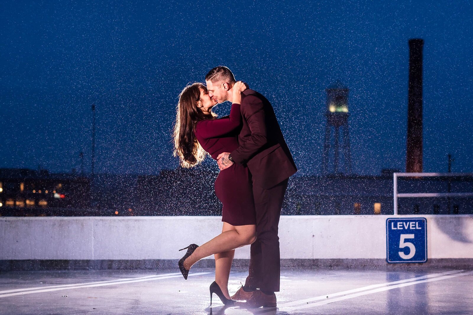 couple dressed in burgundy outfits embrace and kiss in the rain during blue hour