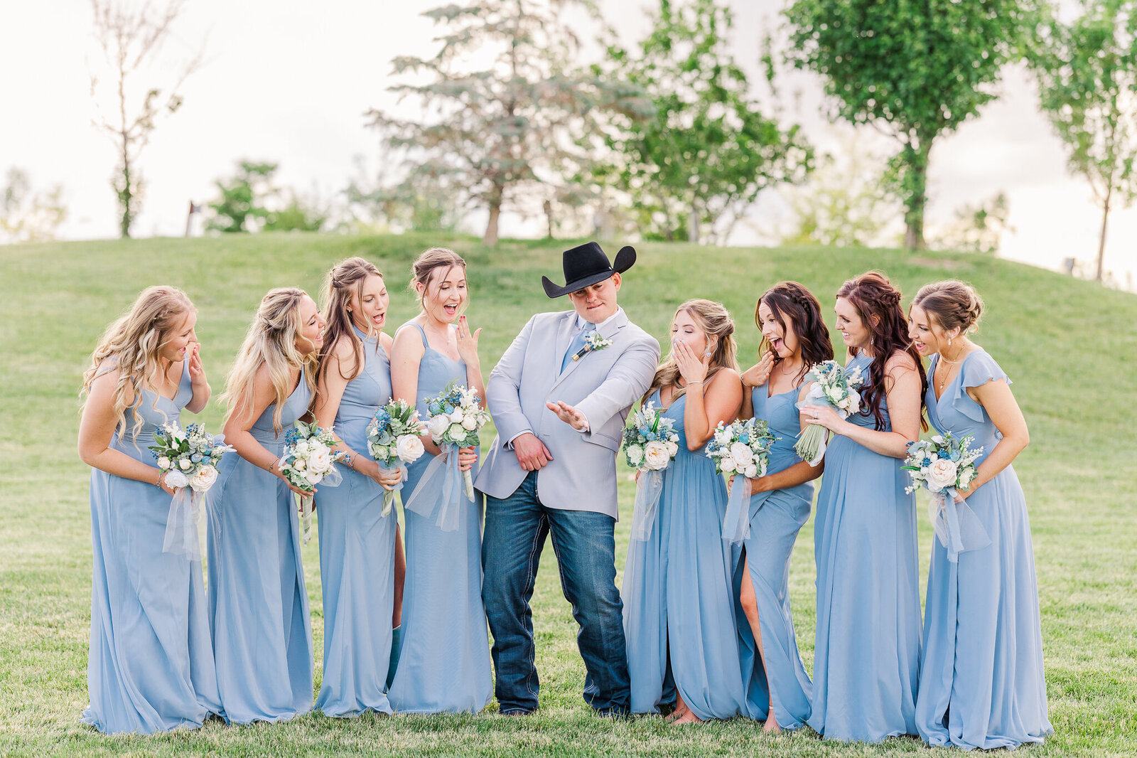 Playful moment as the groom shows off his wedding ring to surprised bridesmaids at a Loma, Colorado wedding