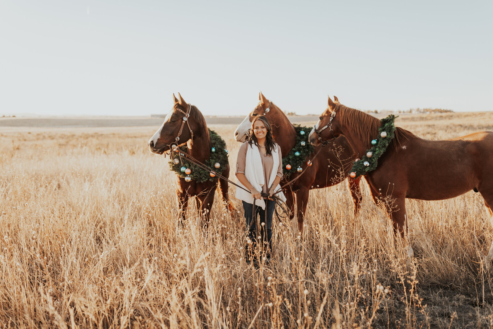 Girl poses with her horses in christmas wreaths for holiday photos