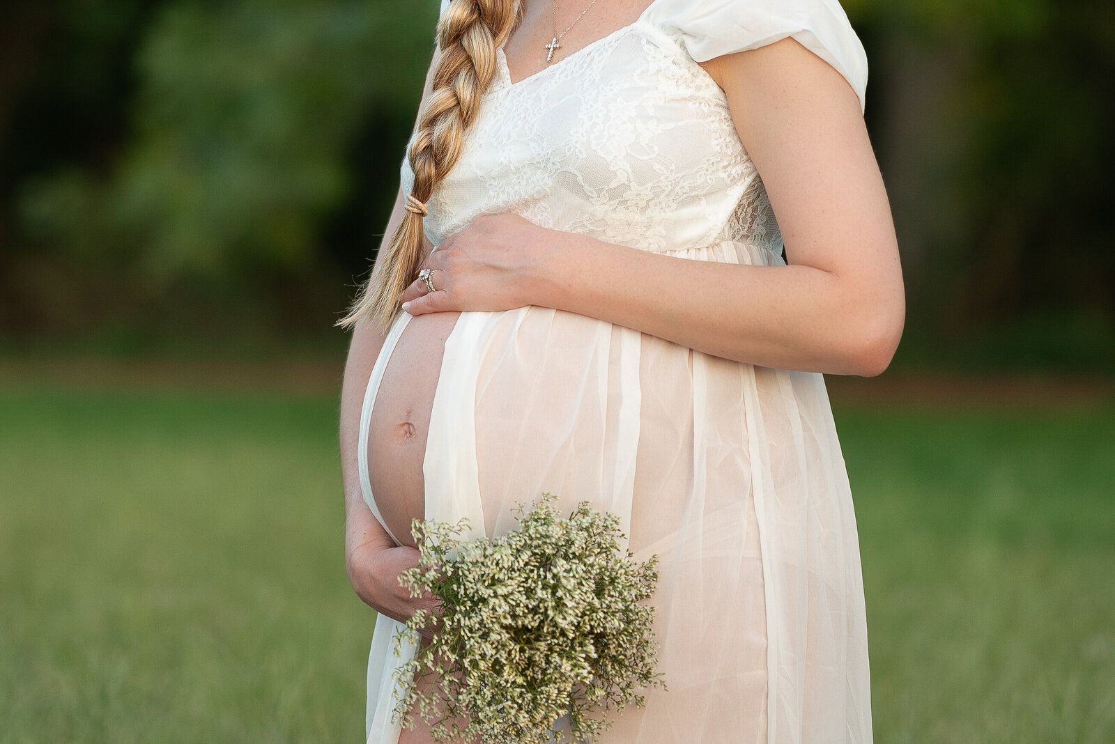 A pregnant woman is  holding her stomach with a bouquet of babies  breath as she poses for her maternity pictures outdoors in Huntsville Alabama