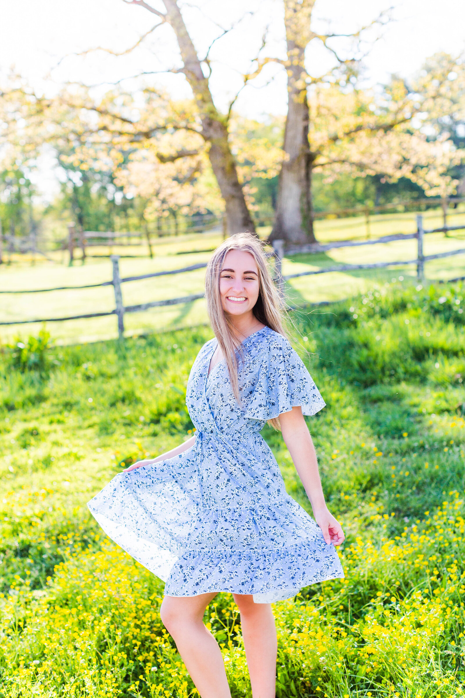 senior in blue dress twirling in field of flowers
