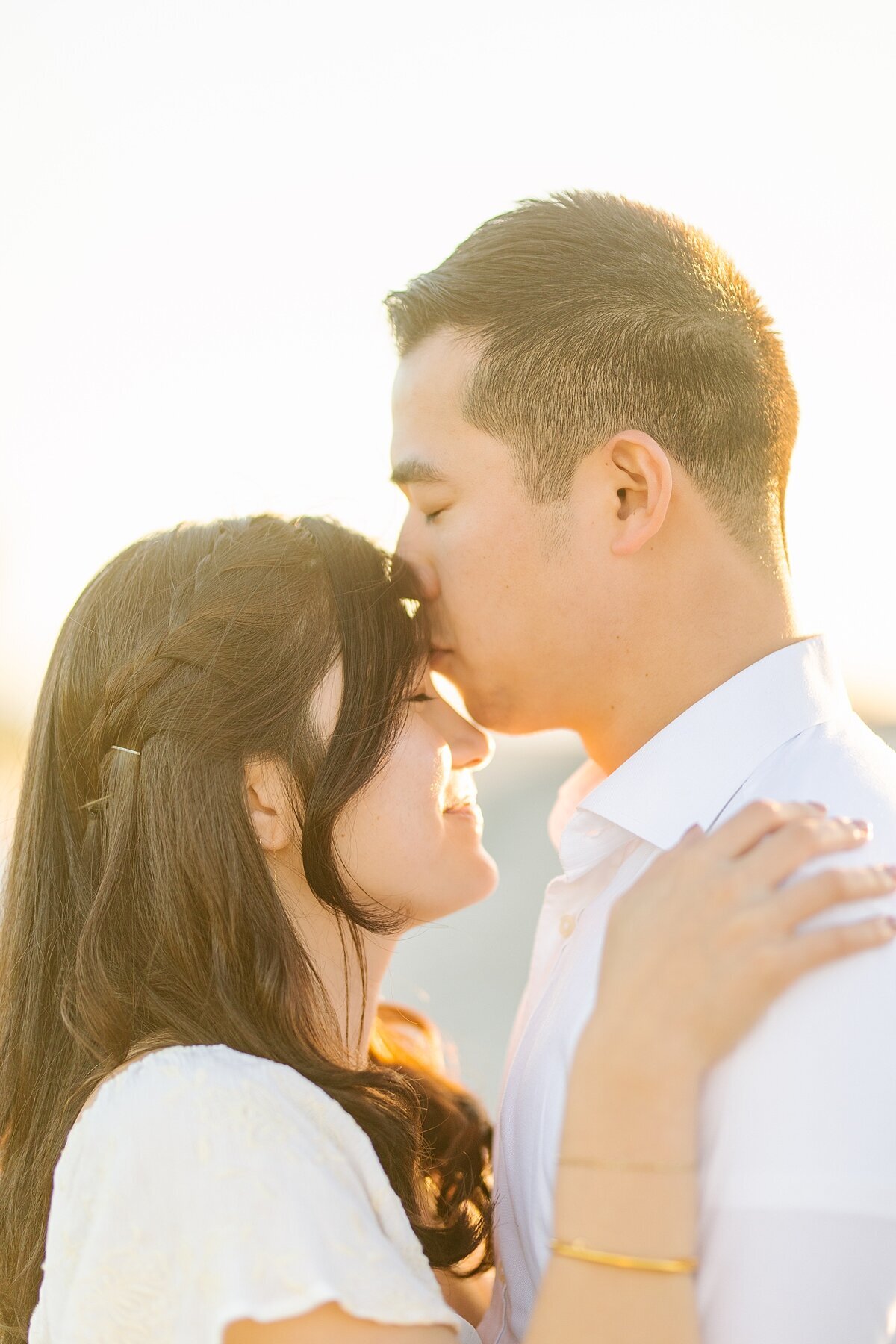 Guy kissing his fiance on the forehead during golden hour portraits.